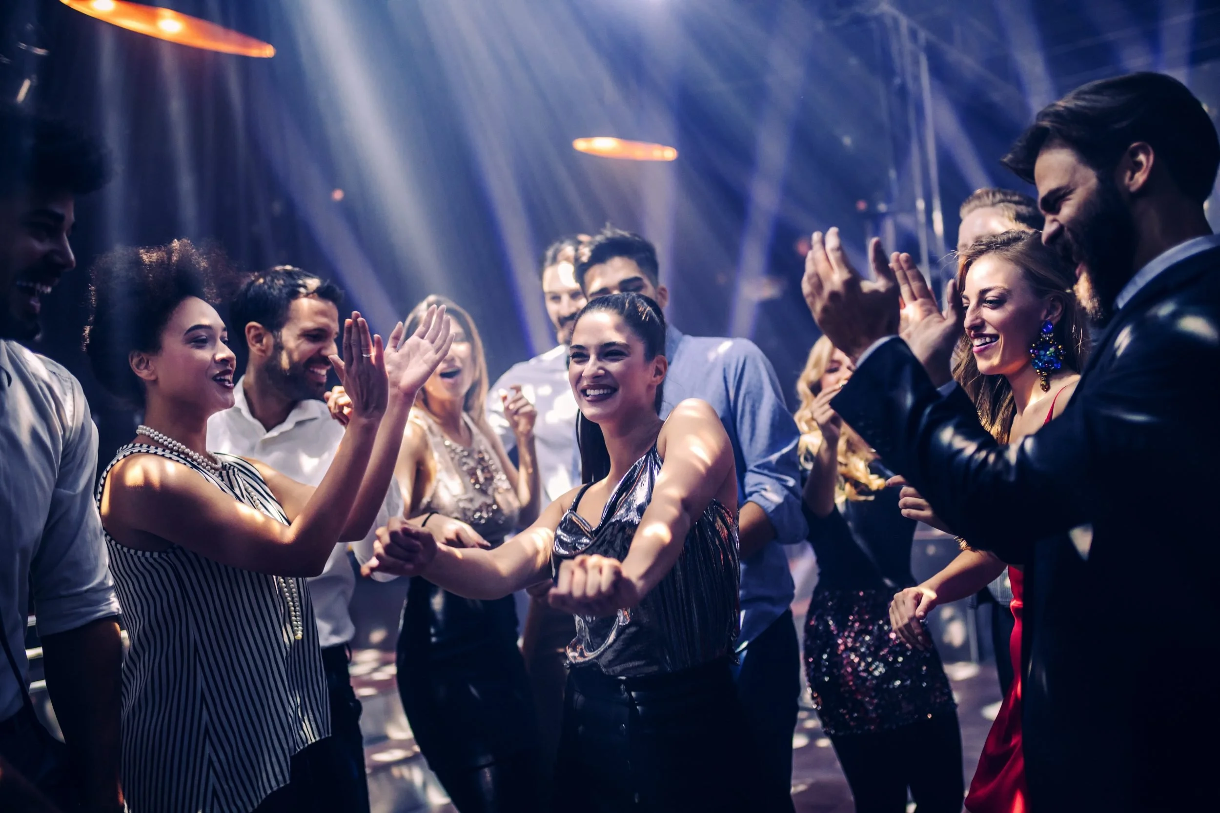 A group of people at a party dancing and smiling under colorful lights.