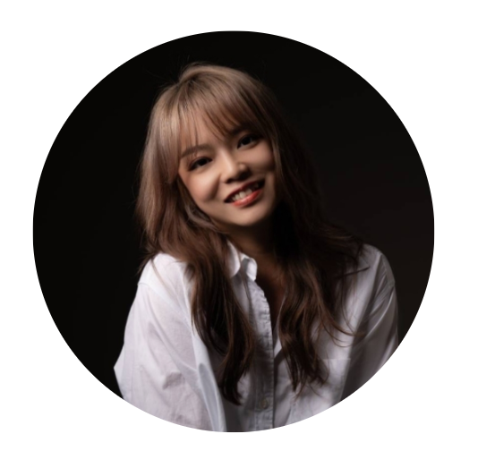 Young woman with long, wavy brown hair and a white shirt, smiling against a black background.