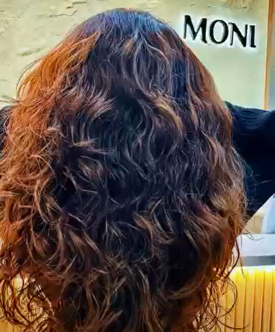 Back view of a woman with curly, brown and black hair, in a hair salon.