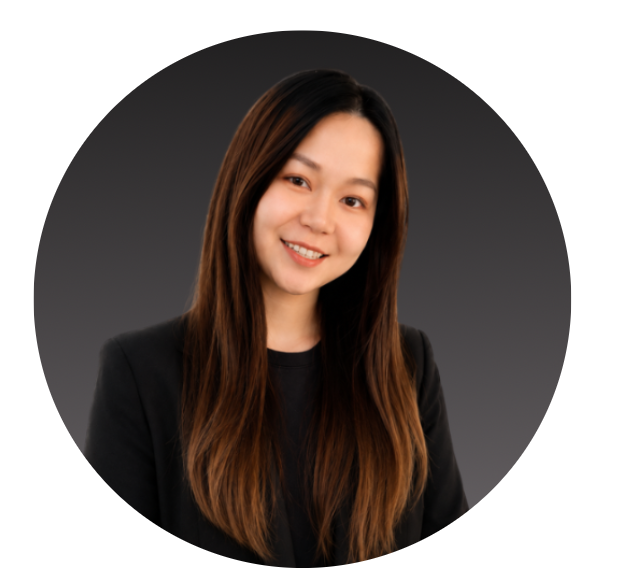 A portrait of a young woman with long brown hair, smiling, wearing a black blazer, against a dark gray background.