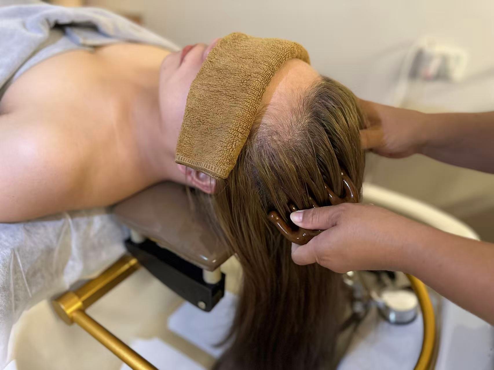 Person receiving scalp massage or hair treatment with heated tool while lying face down on a massage table.