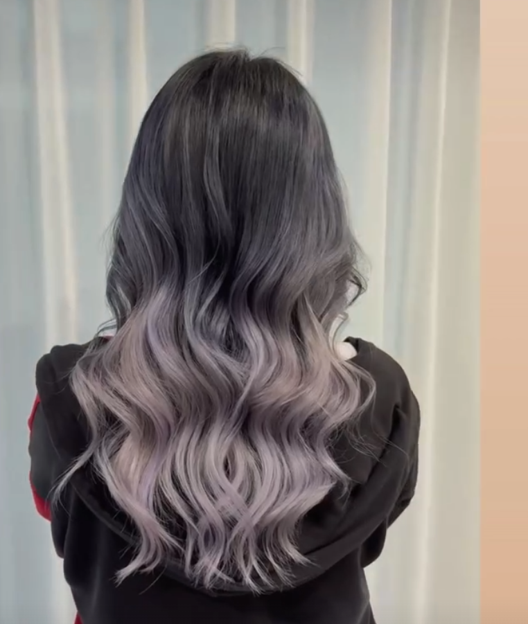 Back view of a woman with long, wavy hair that is dark at the roots and fades into a light lavender color.