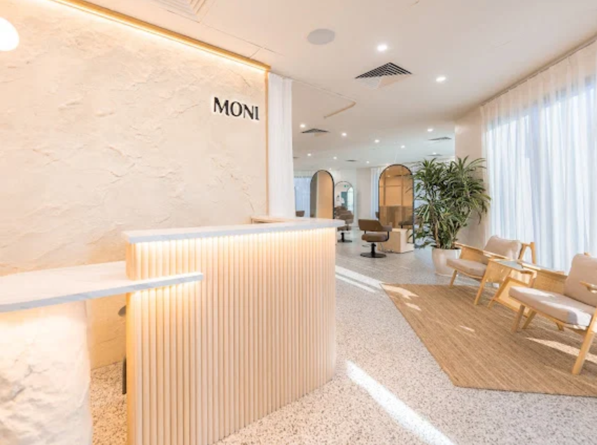 Modern hotel lobby with a reception desk, seating area, and large window with curtains, decorated in neutral tones with plants.
