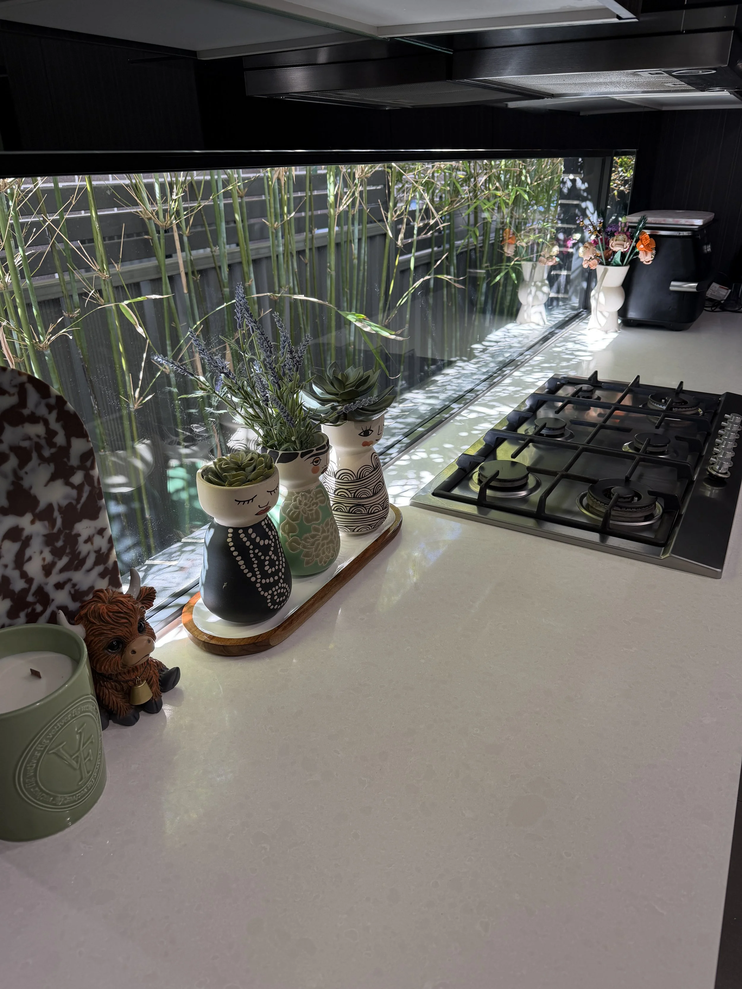 Kitchen counter with decorative plant pots, a candle, a small figurine, a toaster, and a window with bamboo outside.
