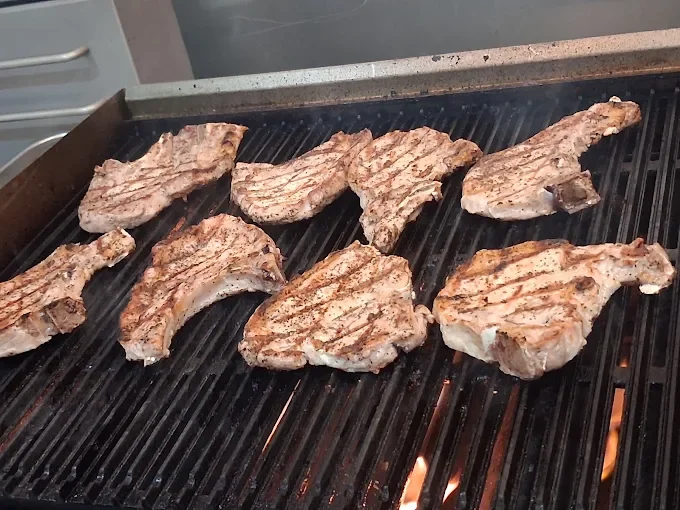 Seven pork chops are grilling on a barbecue grill.