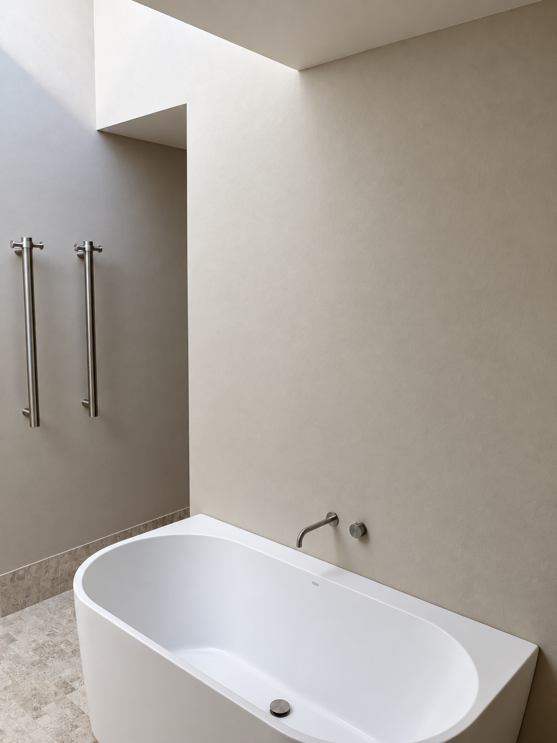 Modern bathroom with a freestanding white bathtub under a beige wall, two vertical towel bars on the wall, and a subtle wall-mounted faucet.