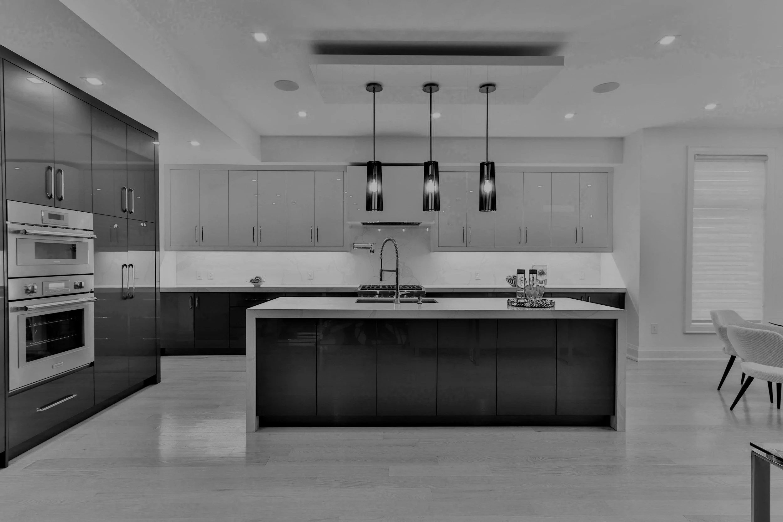 Modern kitchen with white upper cabinets, black lower cabinets, a large island, built-in oven, and pendant lights.