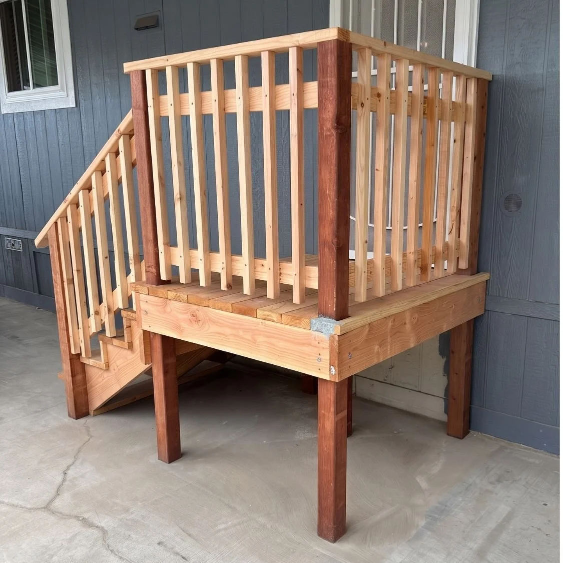 Wooden deck with stairs and railing attached to the exterior of a building with blue siding.