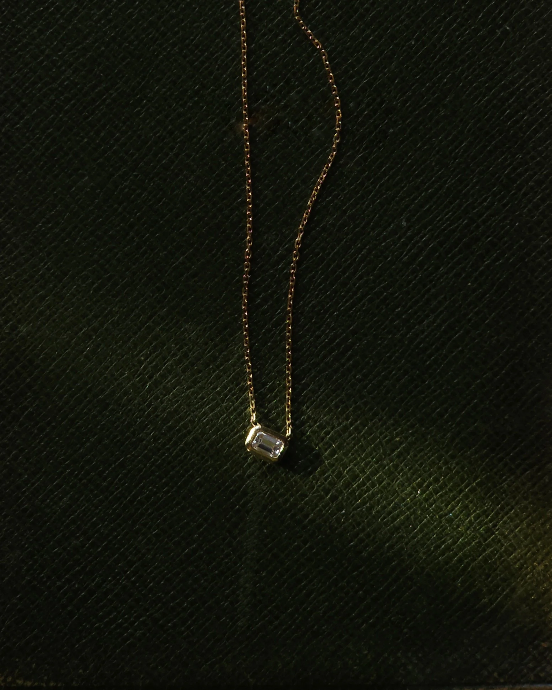Gold chain necklace with a large rectangular clear gemstone pendant on a black textured background.