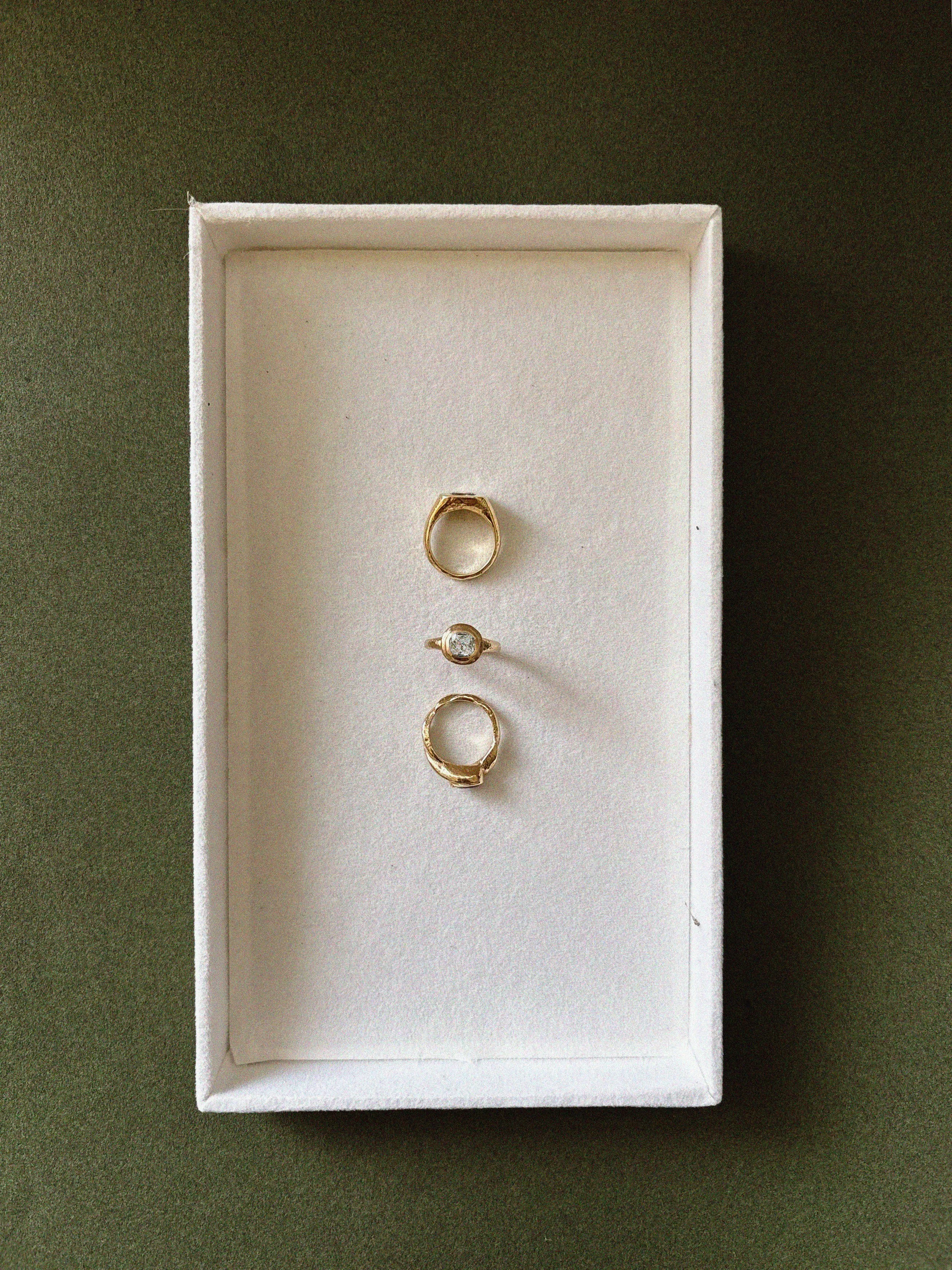 A white jewelry box with three rings inside, placed on a dark green surface.