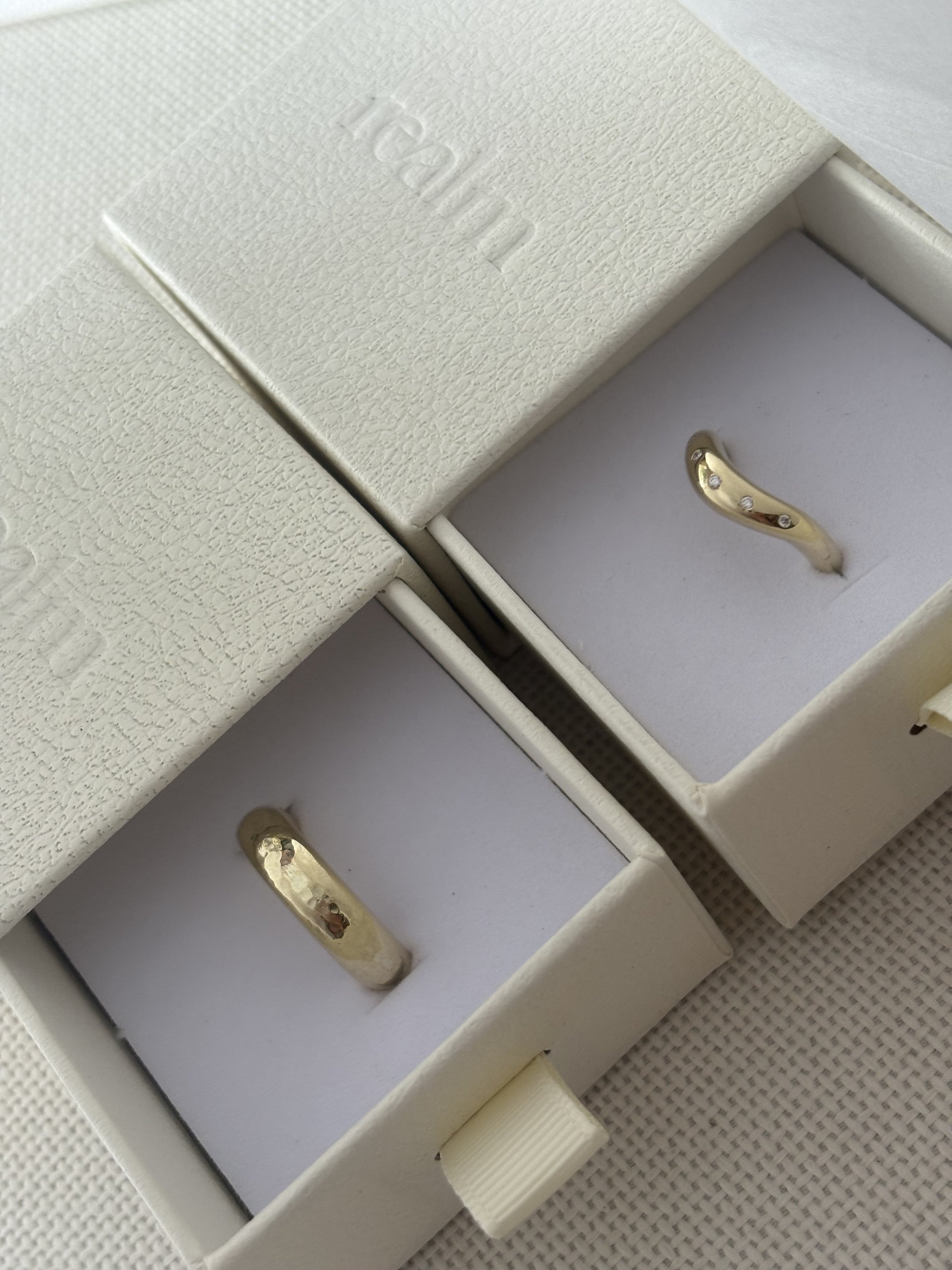 A white jewelry box with a gold ring inside, featuring small gemstones. The jewelry box is open, revealing the ring on a white padded interior.