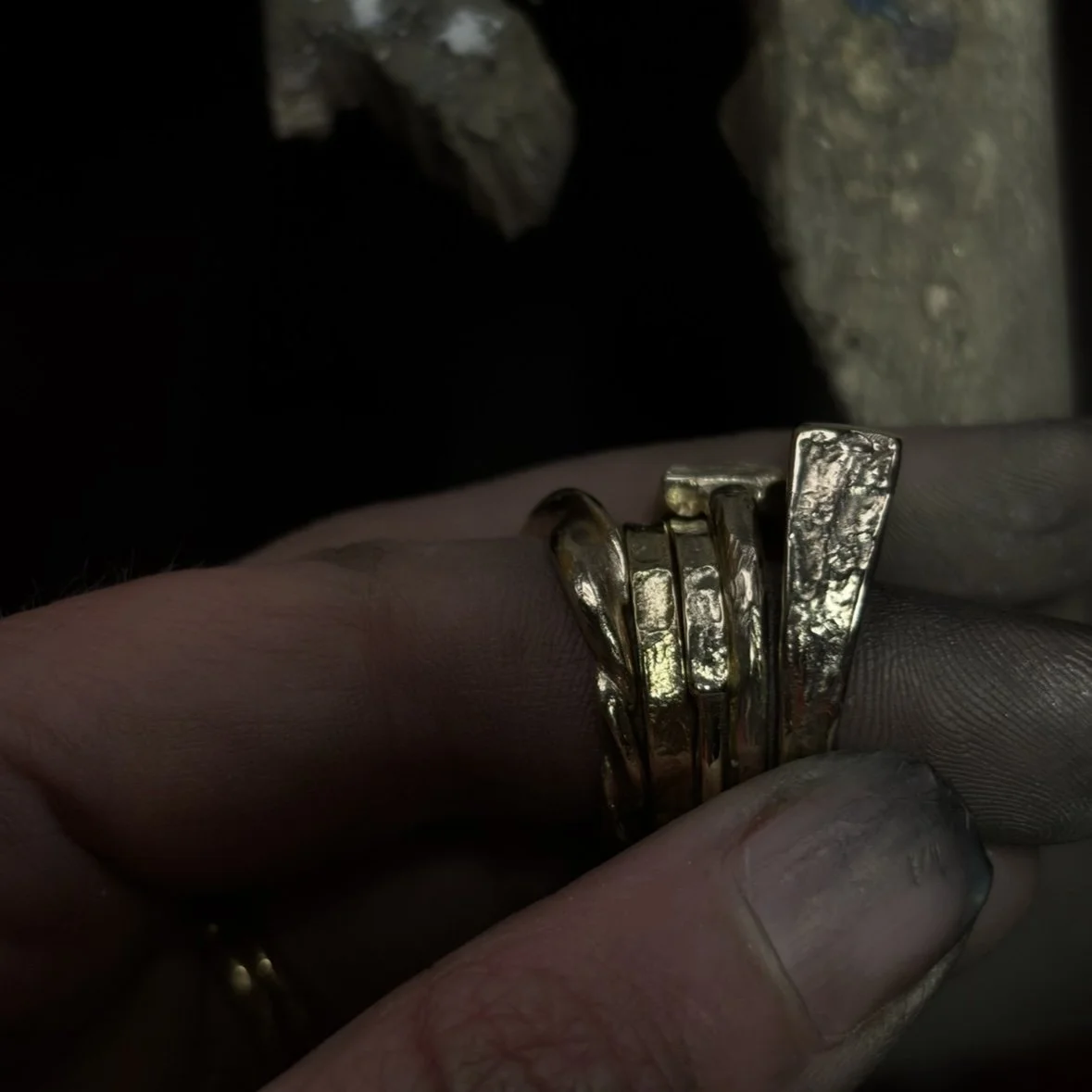 Close-up of a person's hand holding a shiny, textured gold ring with a layered, abstract design.