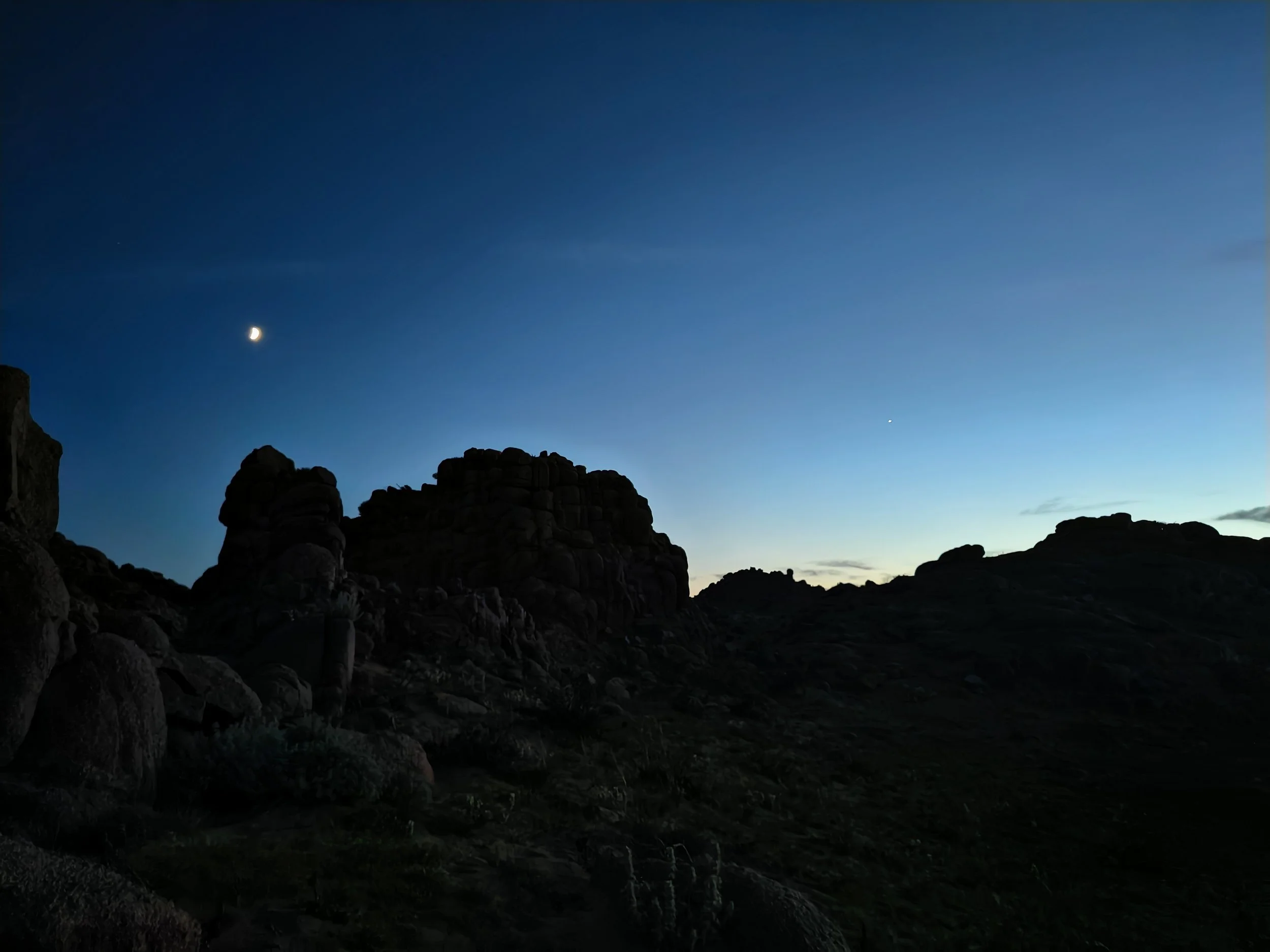 Night sky with a crescent moon and a single bright planet or star, rocky terrain silhouette in the foreground.