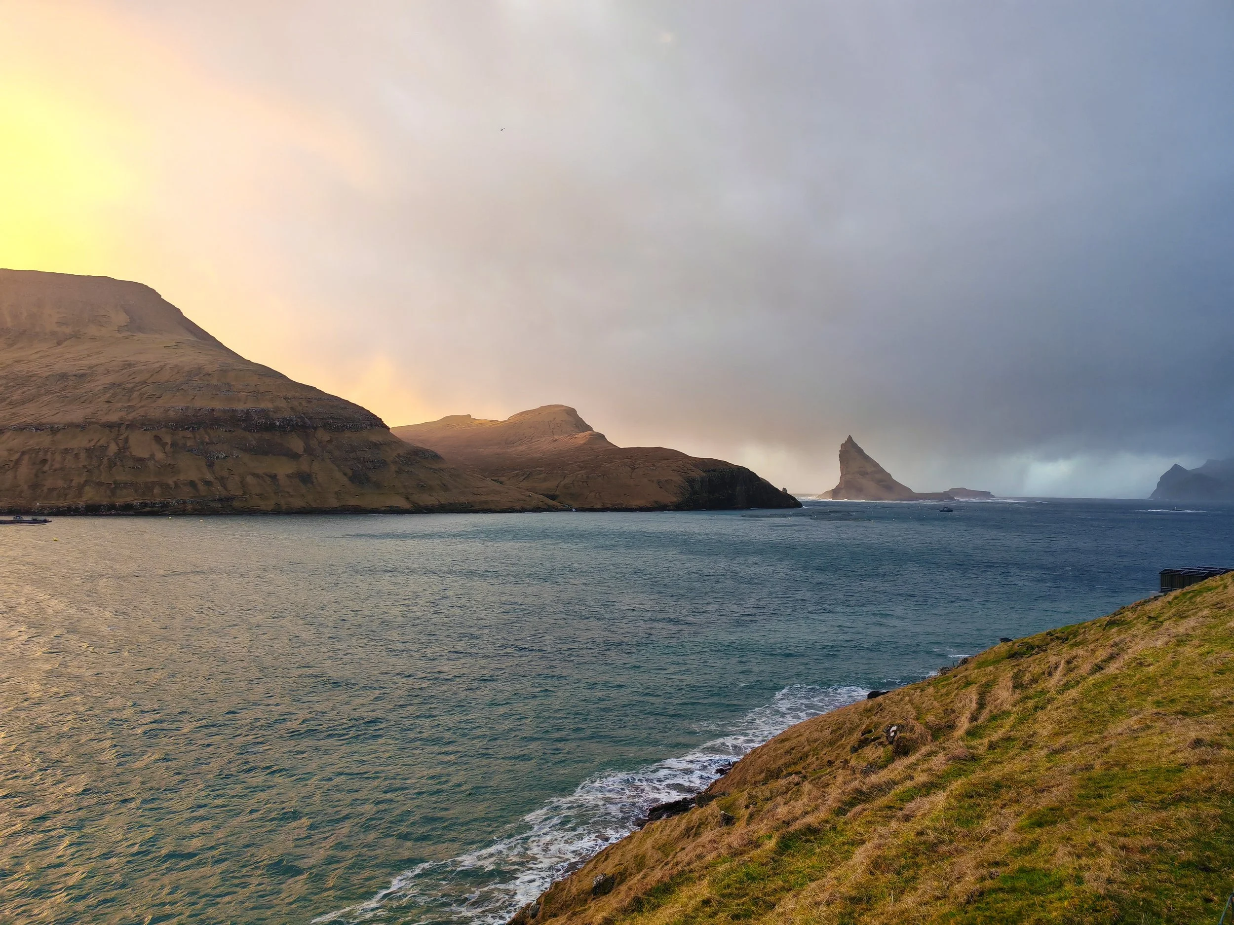 Scenic view of rugged coastal cliffs and rock formations extending into the ocean, under a cloudy sky at sunset or sunrise.