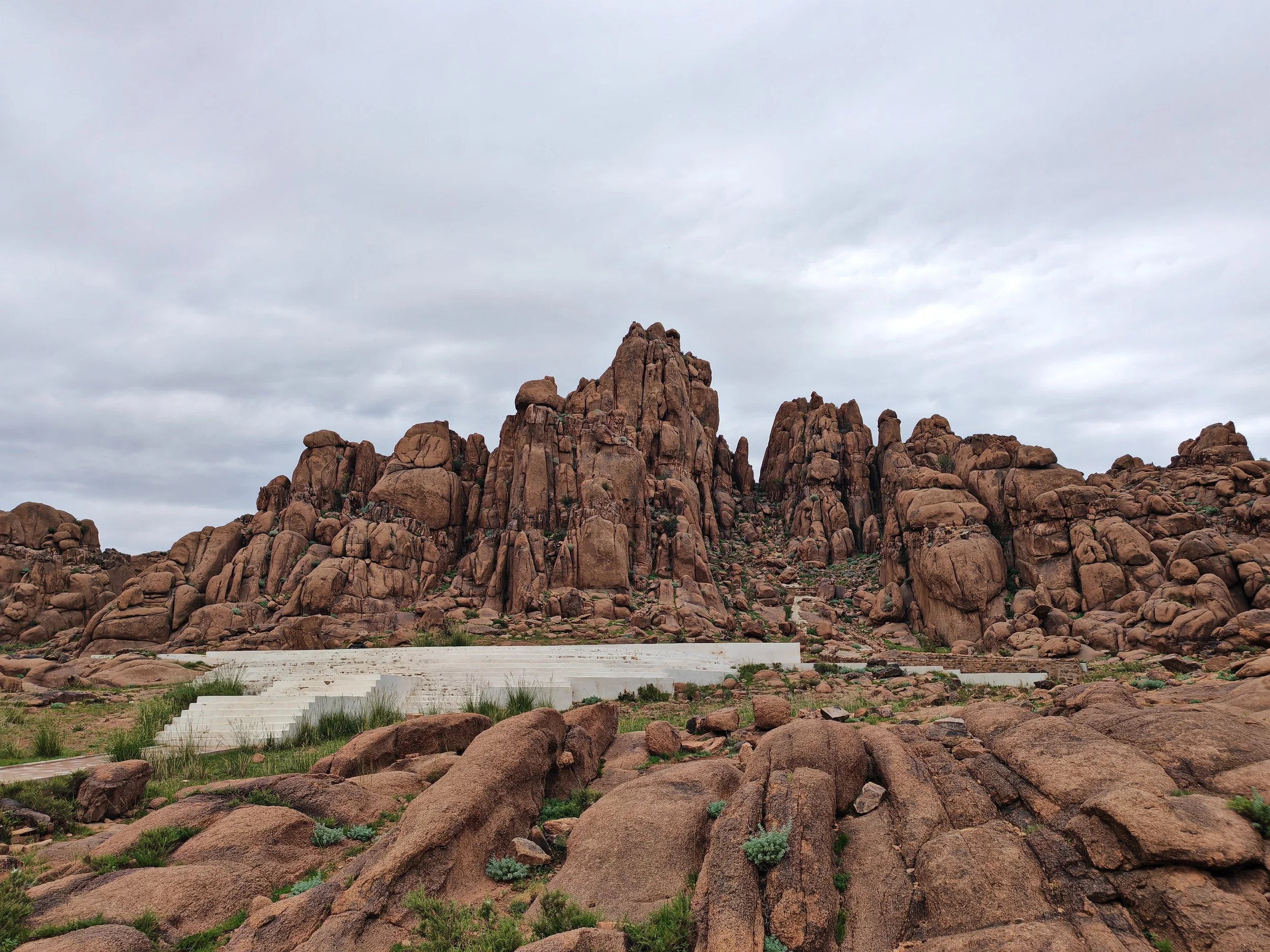 A large rock formation with rounded boulders in a desert landscape under a cloudy sky.