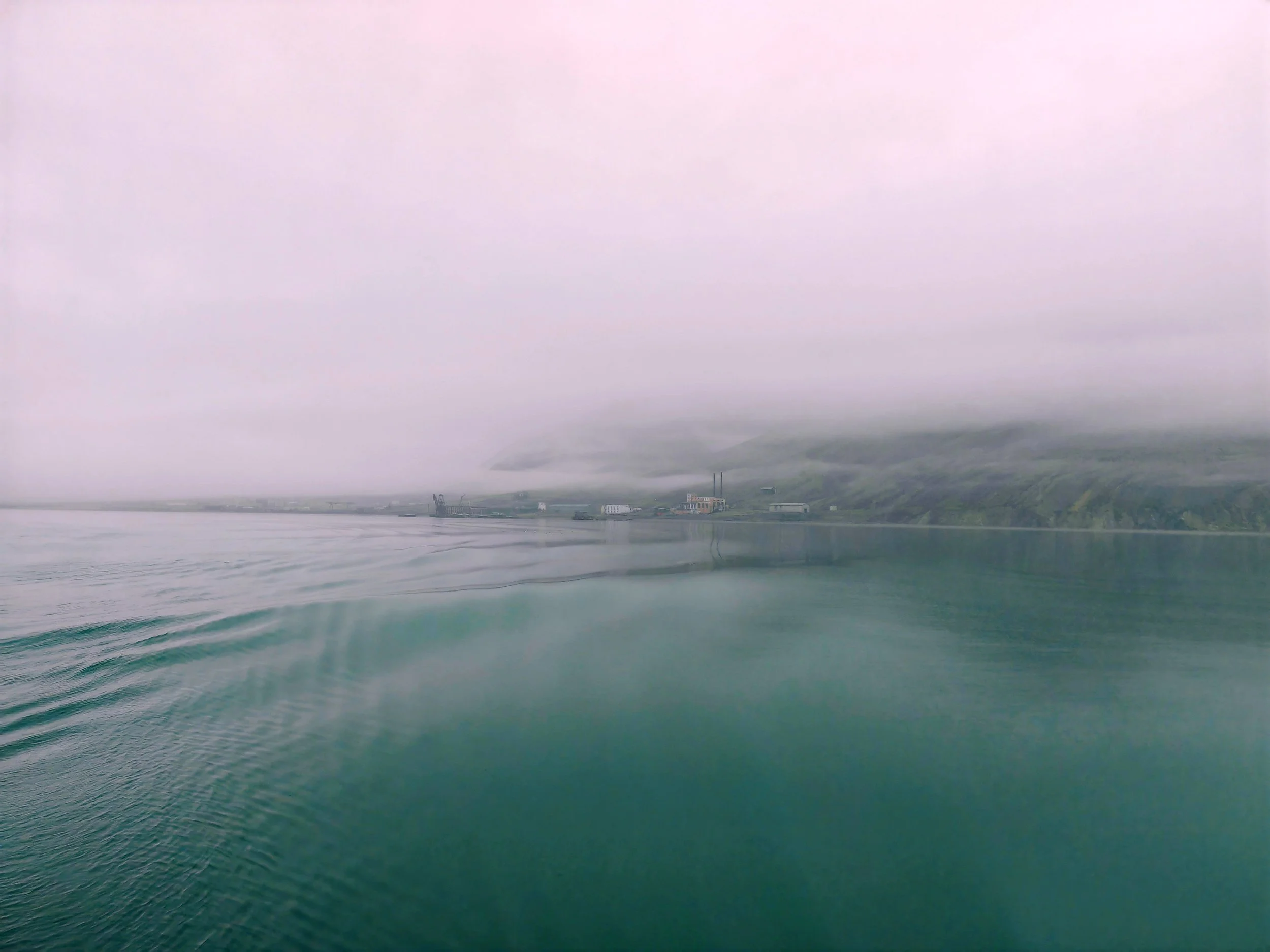 Overcast sky over a calm body of water with a distant industrial area and hills.