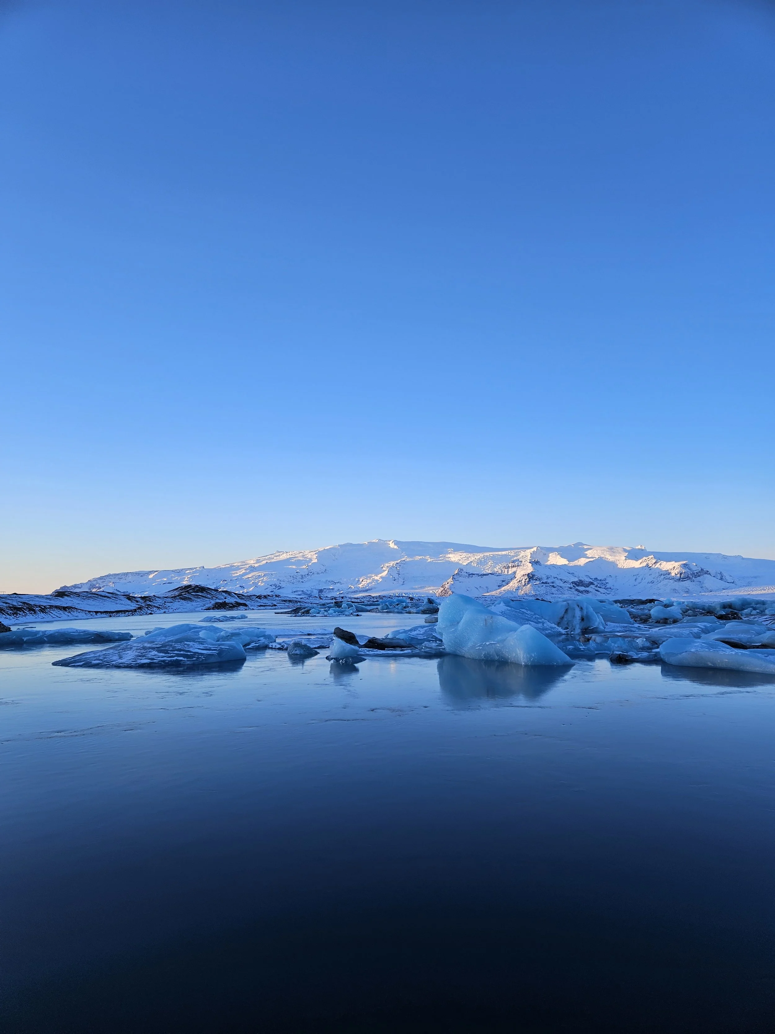 A snowy mountain landscape with icebergs floating in the water, under a clear blue sky.