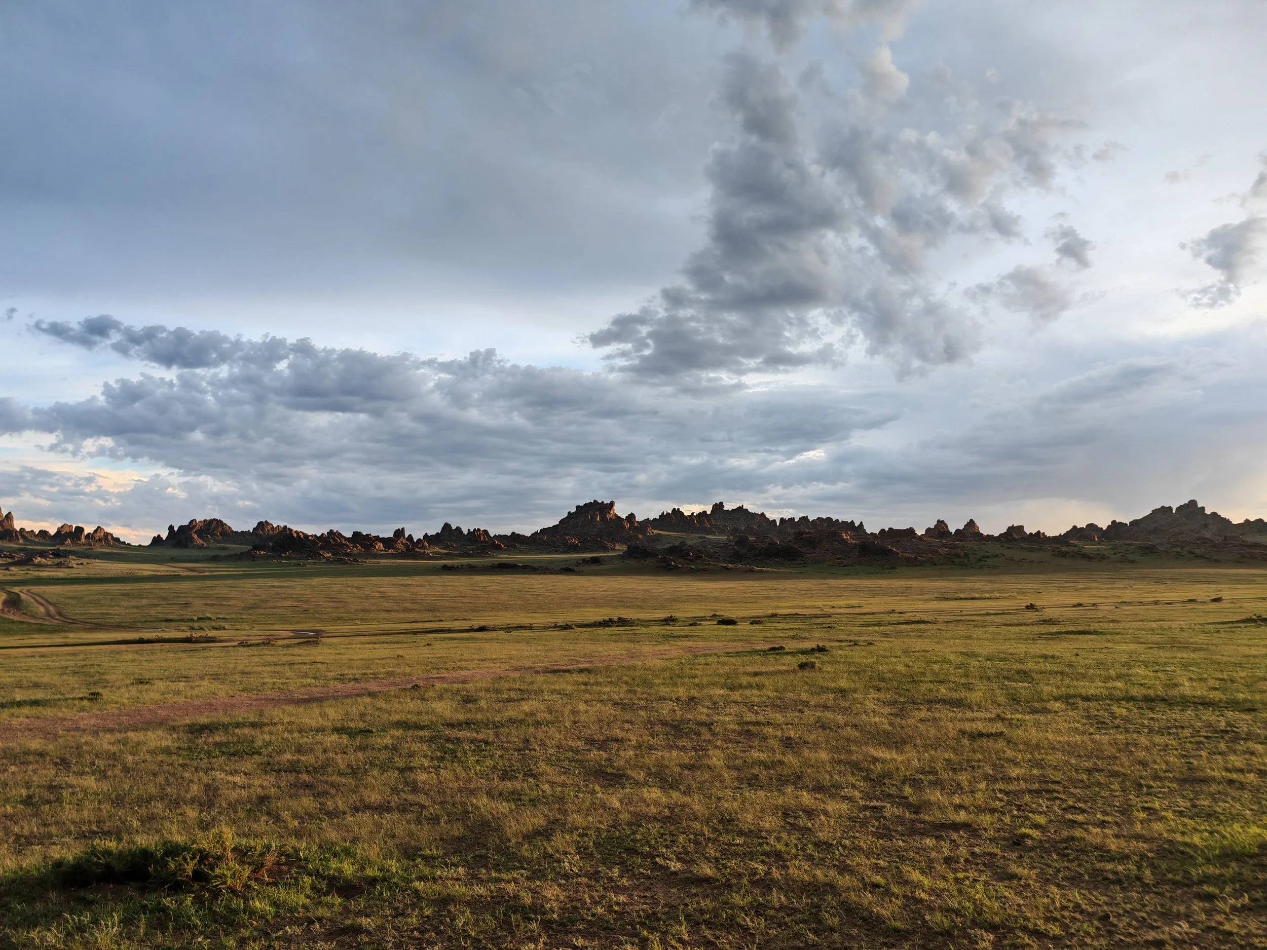 Scenic view of a wide grassy plains with rocky hills in the distance under a cloudy sky.