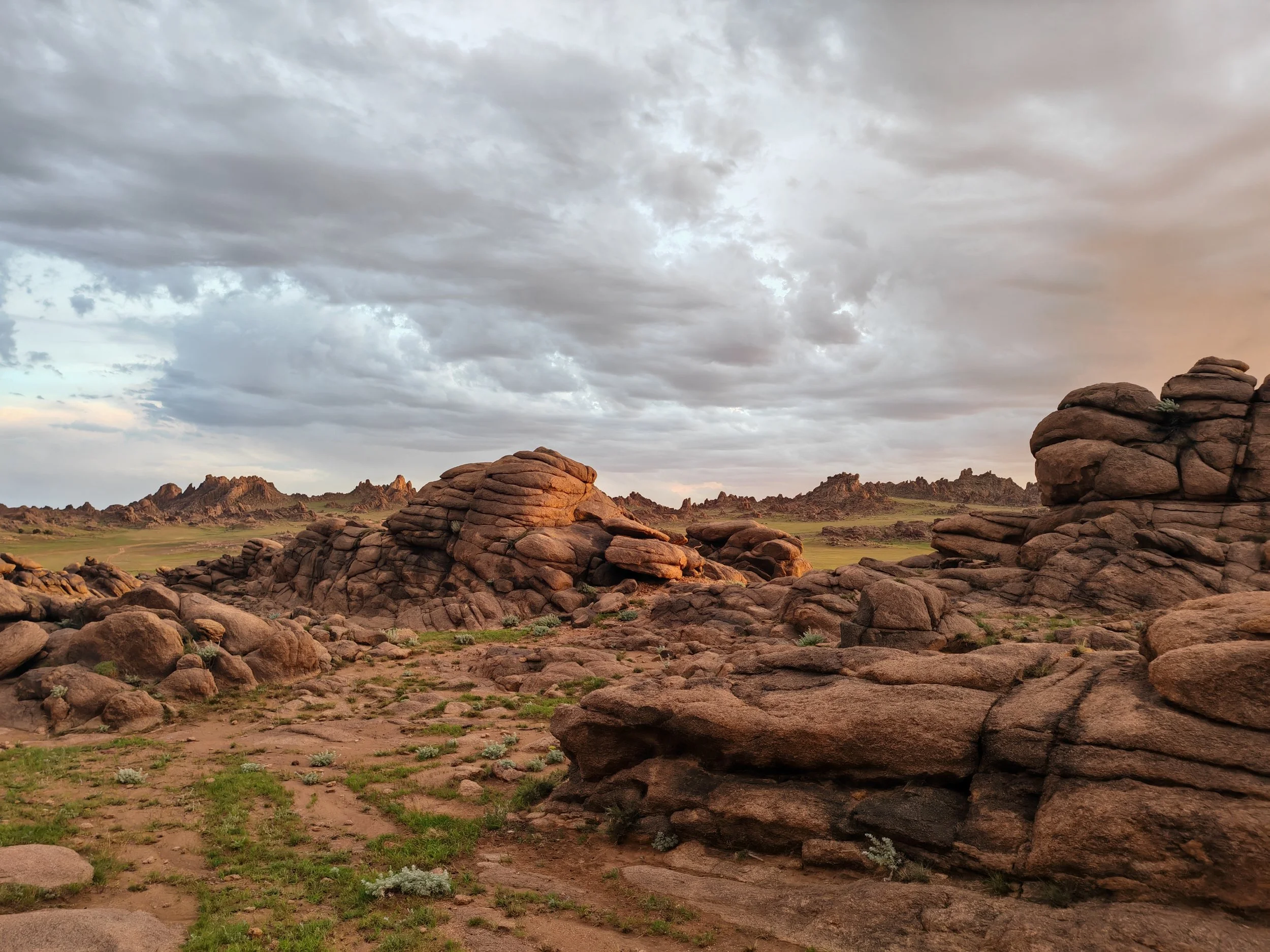 Martian landscape with large rock formations, green patches, and a cloudy sky.