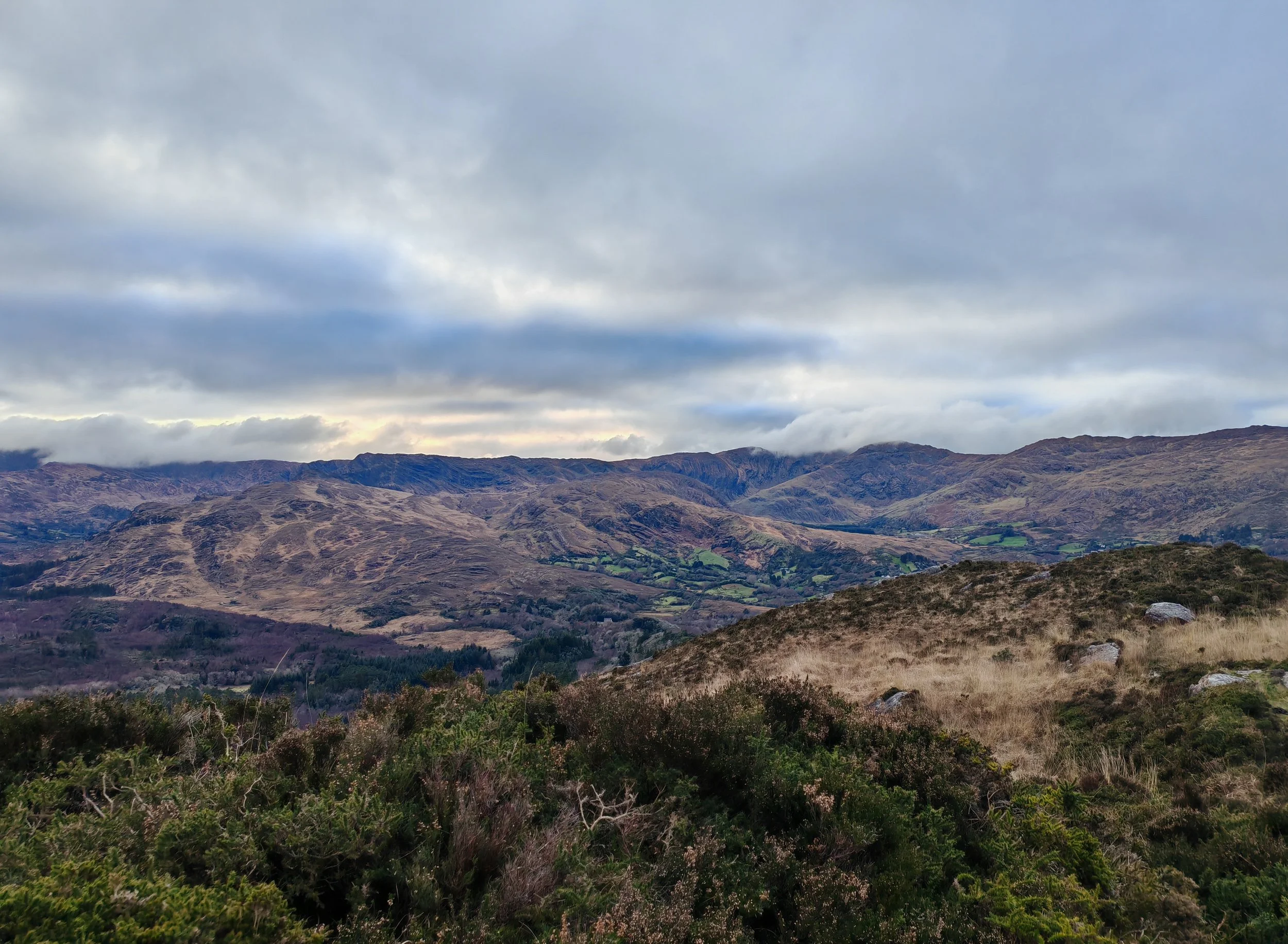 Mountain landscape under a cloudy sky with rolling hills and patches of greenery.