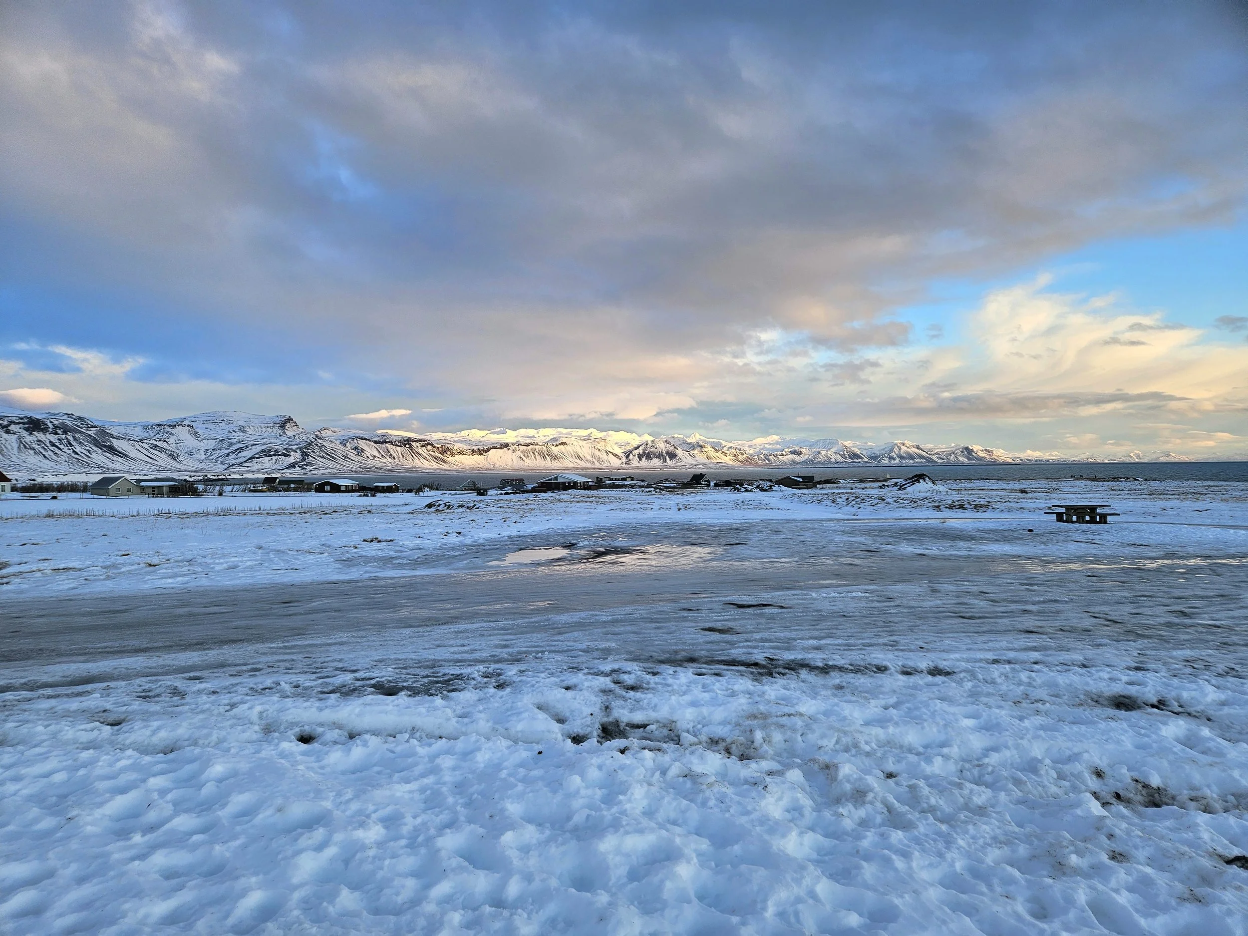 Snow-covered landscape with mountains in the distance under a partly cloudy sky.