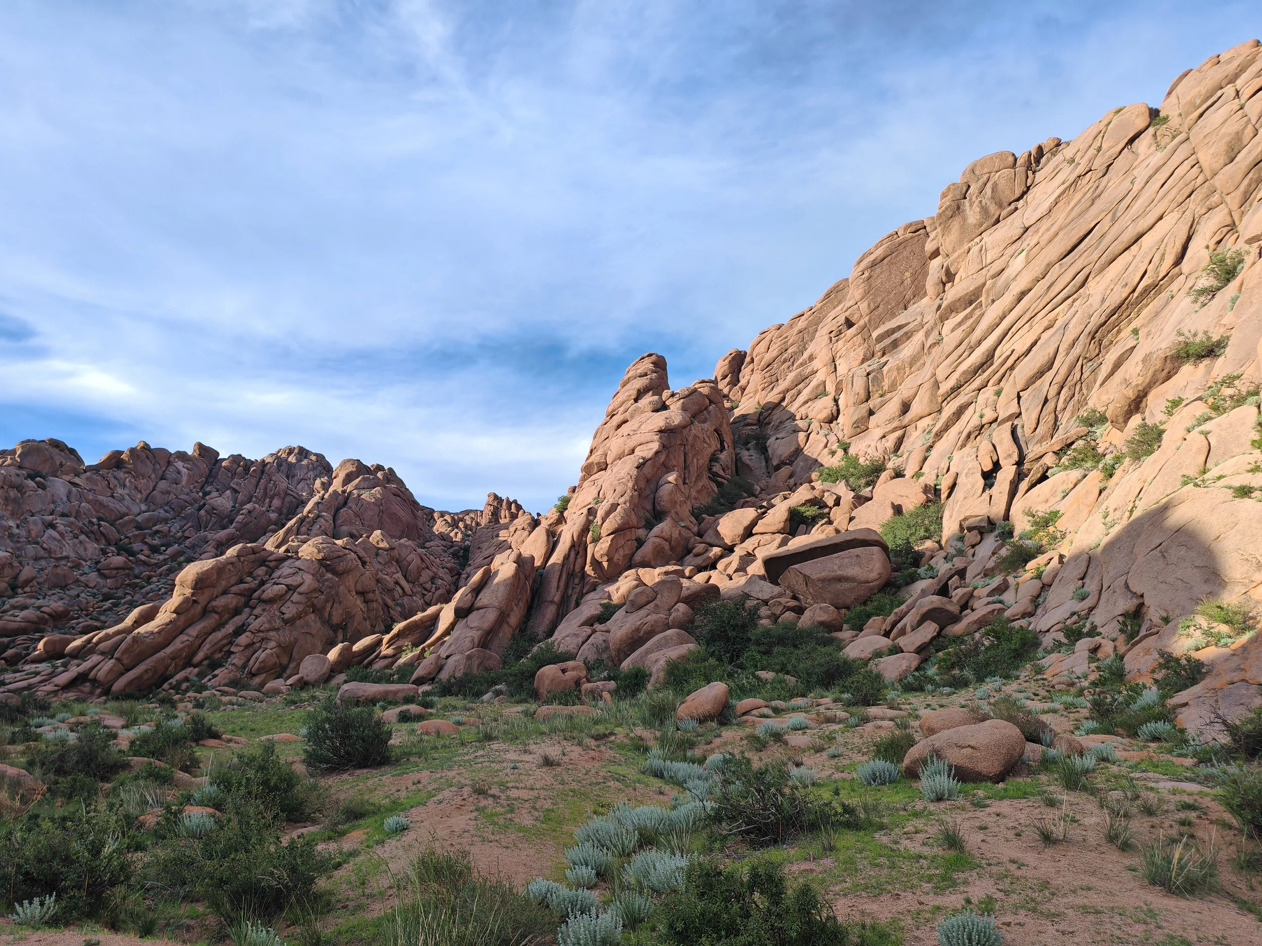 Rock formations on a desert landscape with sparse greenery under a partly cloudy sky.