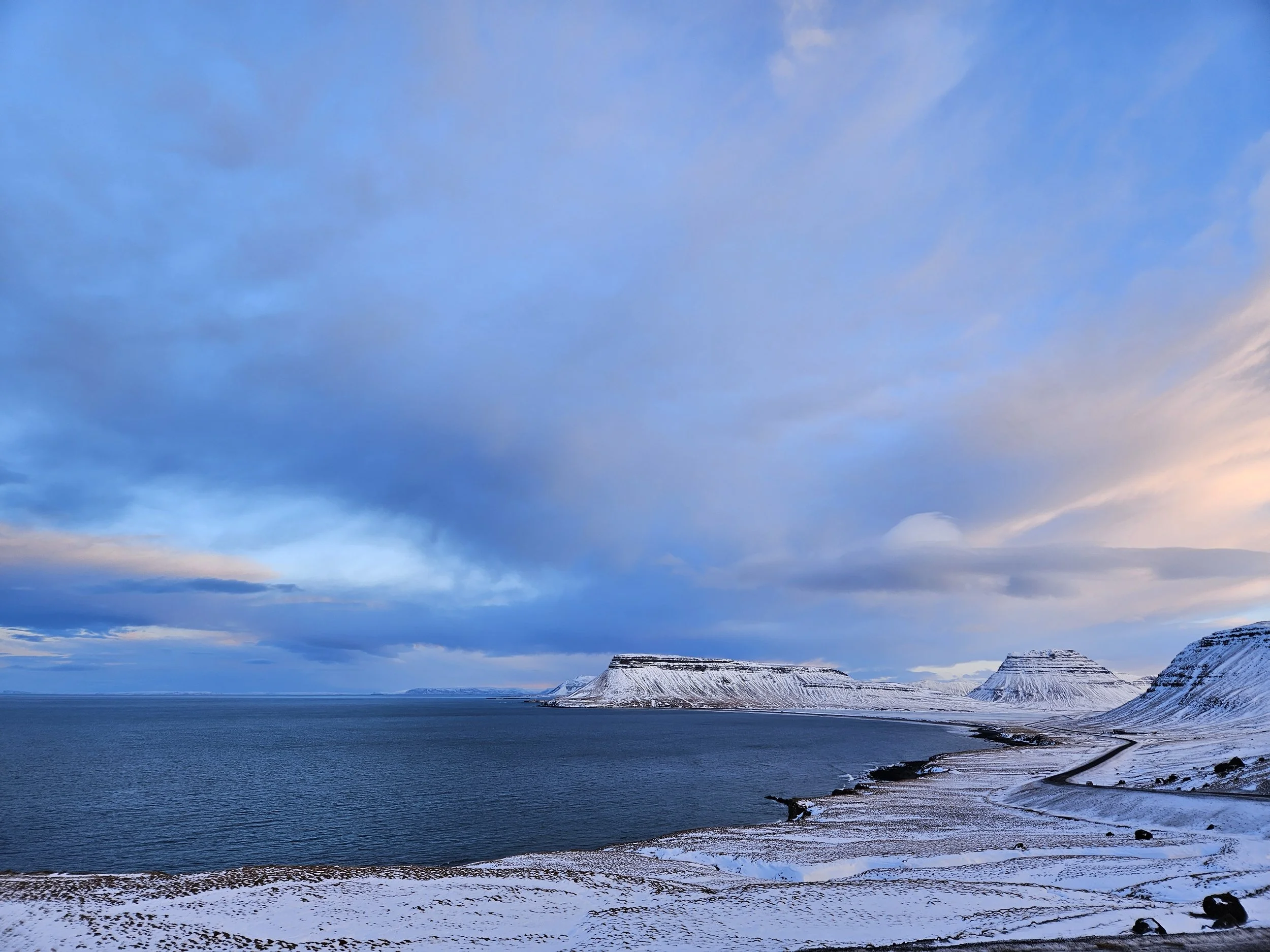 Snow-covered mountains next to a body of water with a cloudy sky overhead.