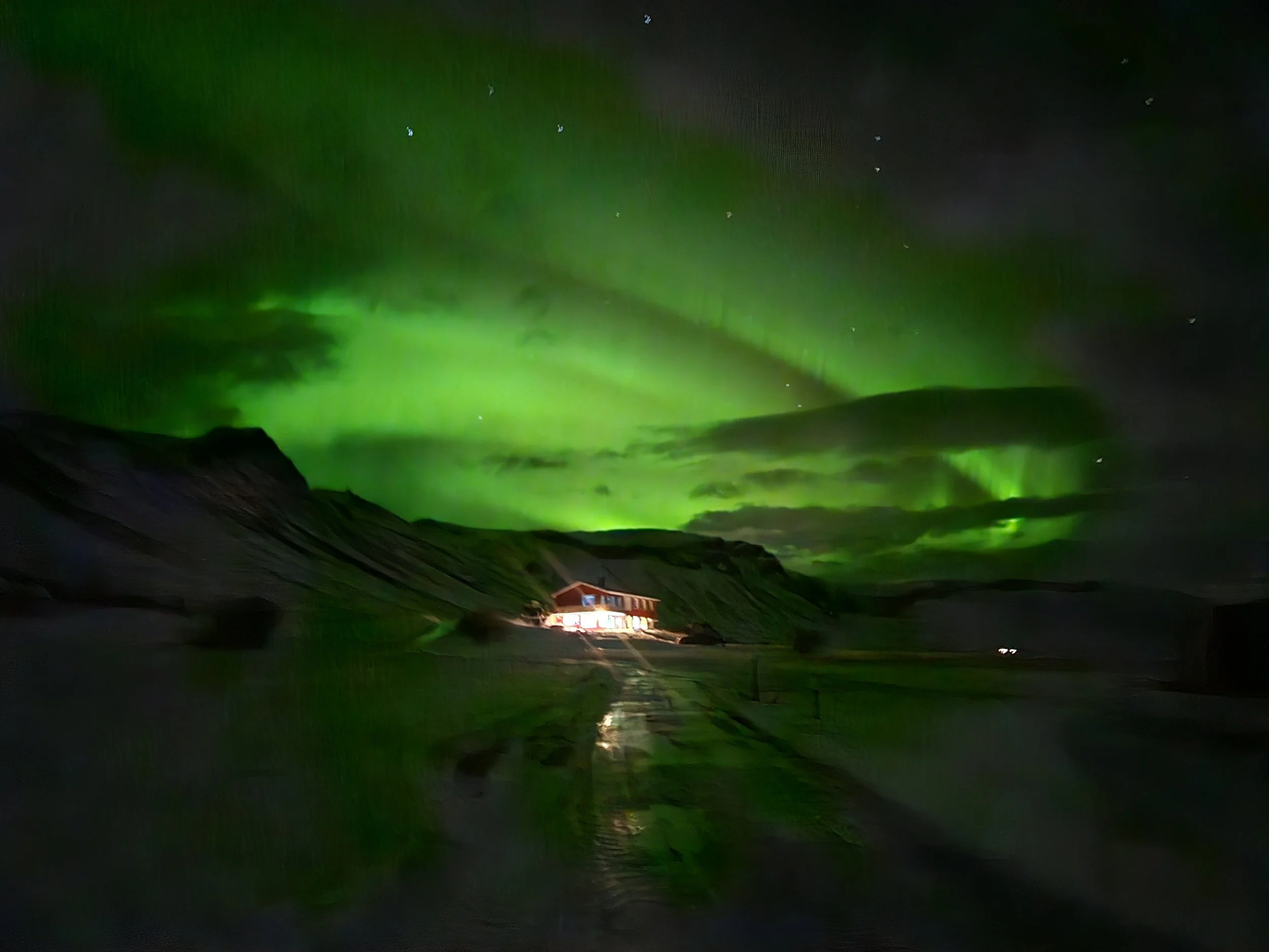Northern lights illuminating a night sky over a dark landscape with a building at the bottom.