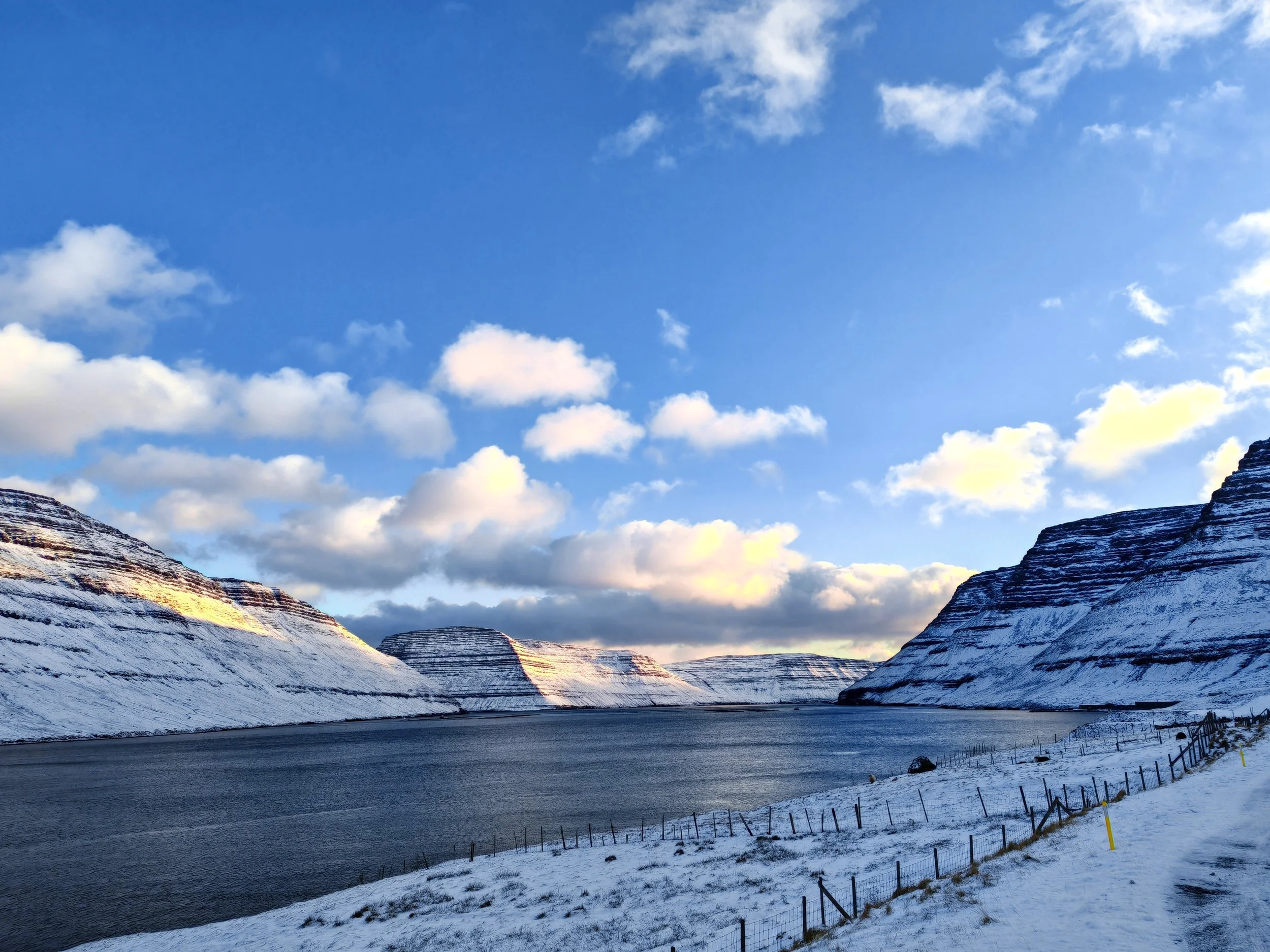Snow-covered mountains beside a winding road under a partly cloudy sky.