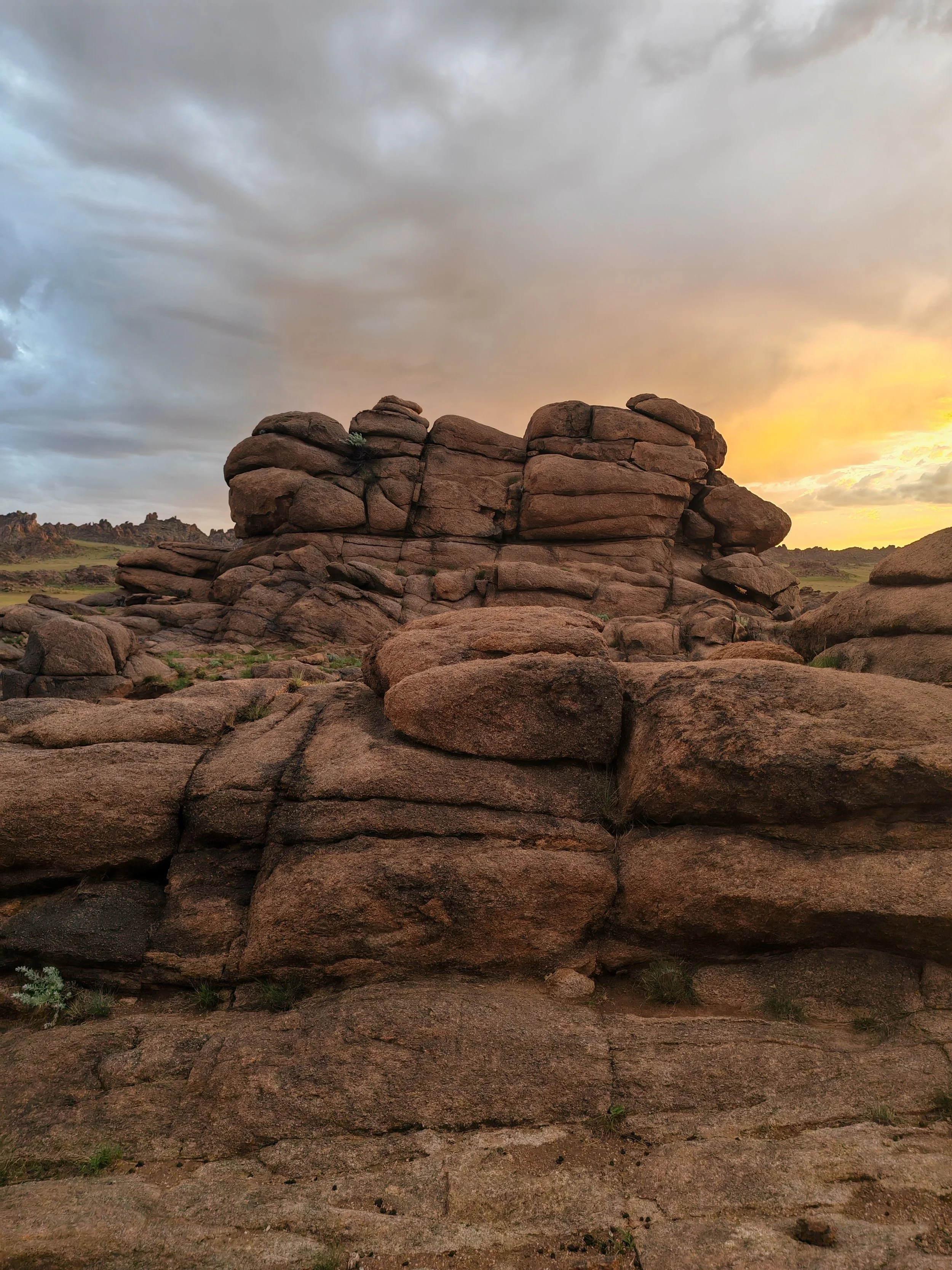 A landscape with large reddish-brown rocks and weathered formations under a cloudy sunset sky.