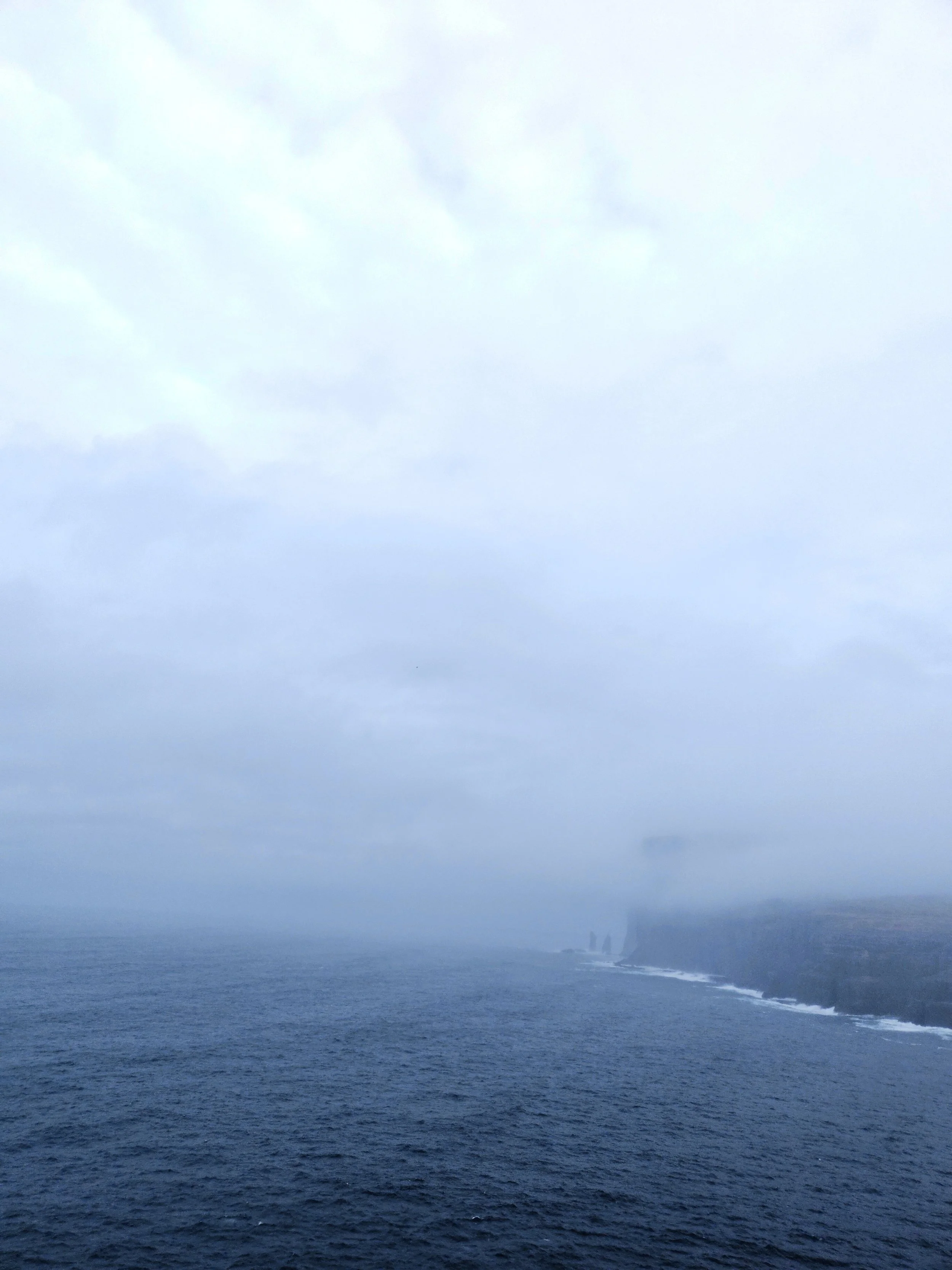 Ocean waves crashing on cliffs with cloudy sky above.