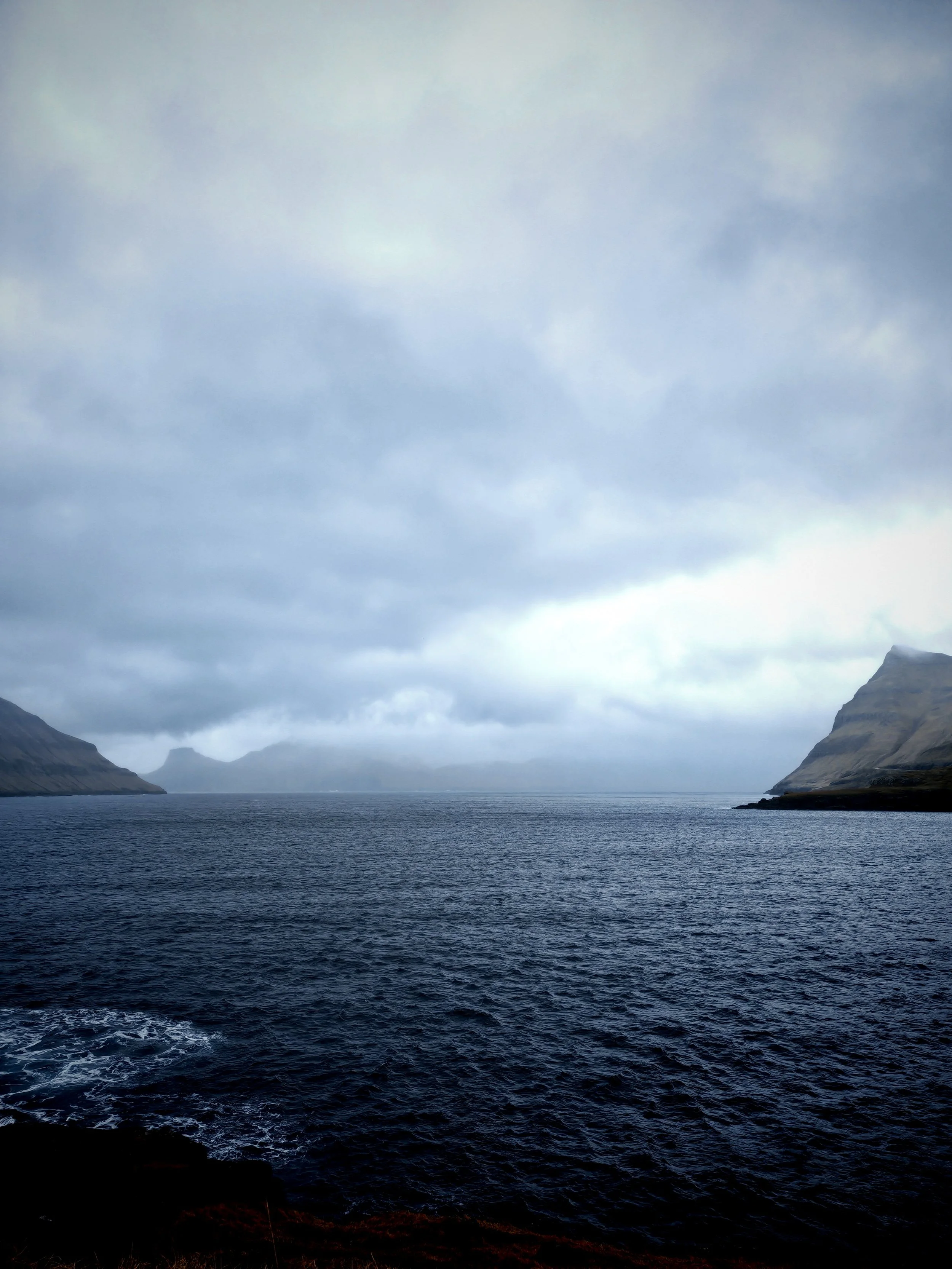 A landscape view of a body of water with mountains in the distance under a cloudy sky.