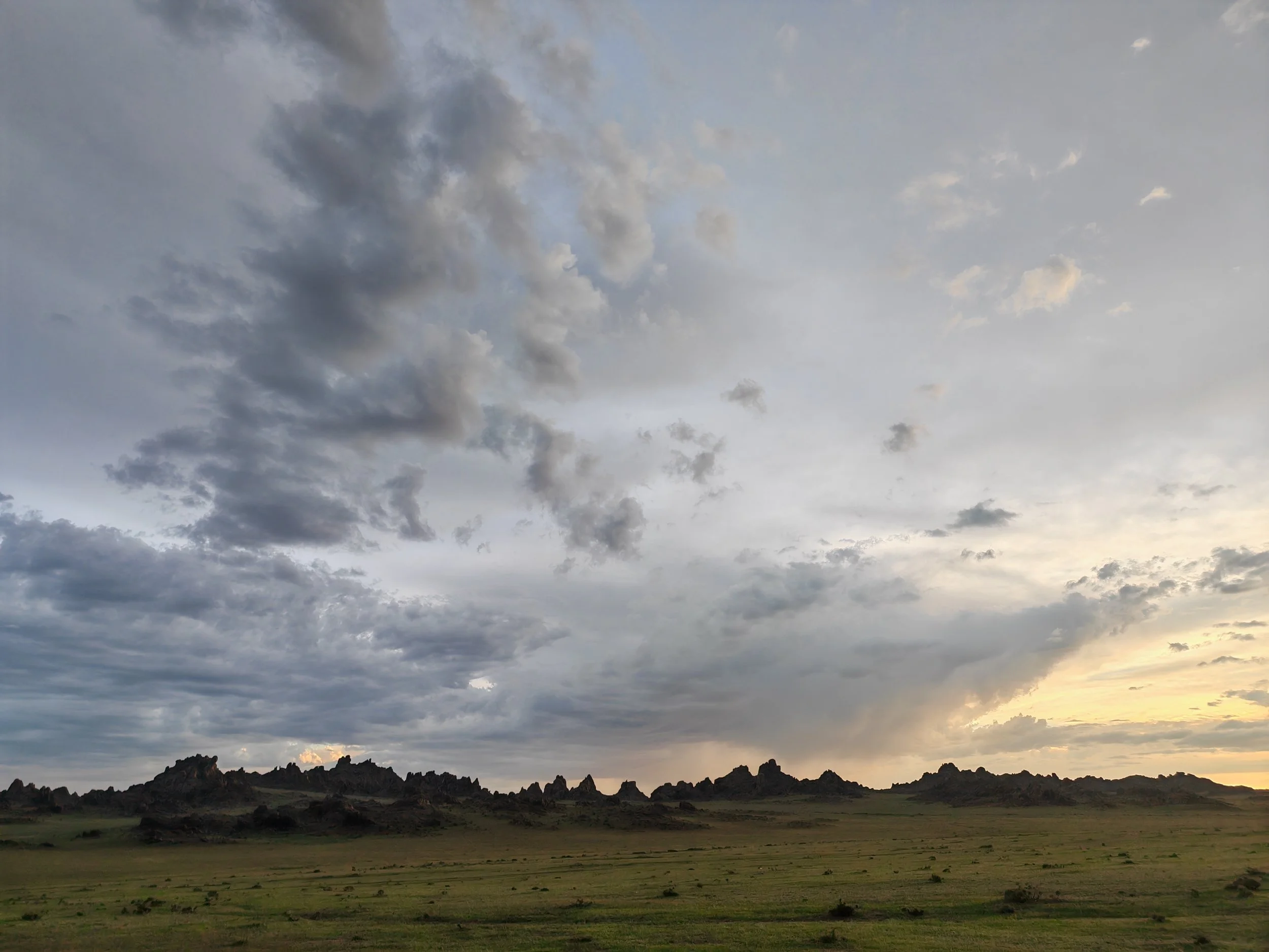 A landscape scene with a cloudy sky, mountains with rocky peaks, and a green grassy plain in the foreground.