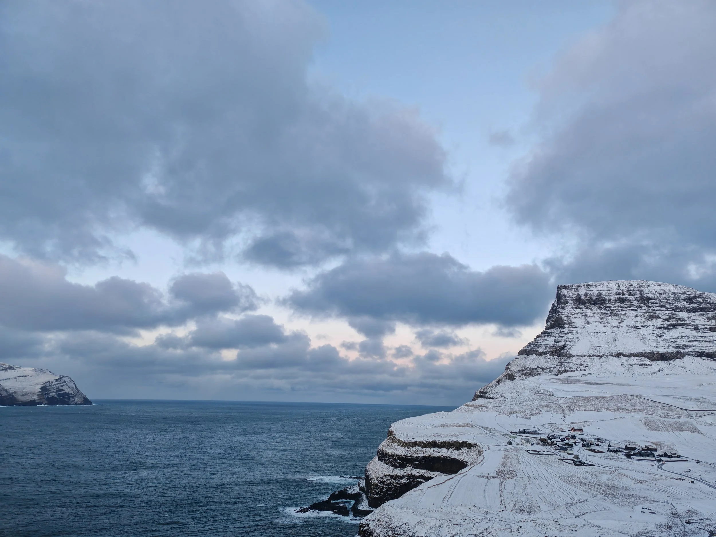 Snow-covered cliffs and a mountain near the ocean under a cloudy sky.