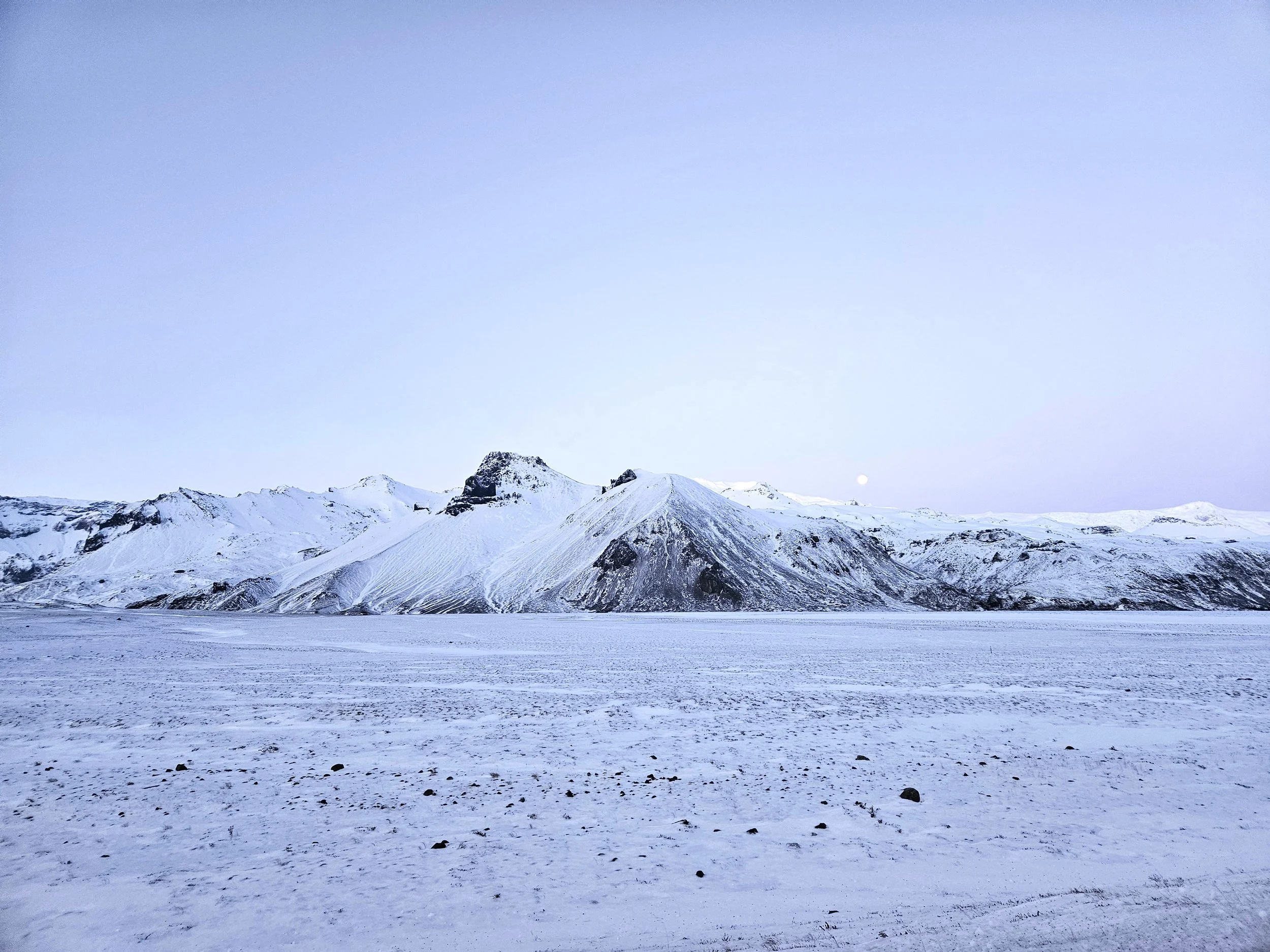 Snow-covered mountain range under a clear blue sky with faint stars visible.