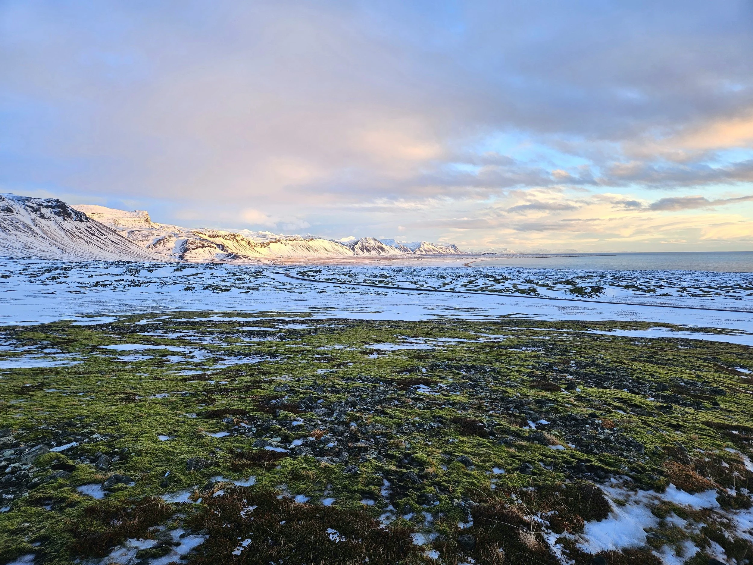 Scenic view of snow-covered mountains and coastline with cloudy sky.