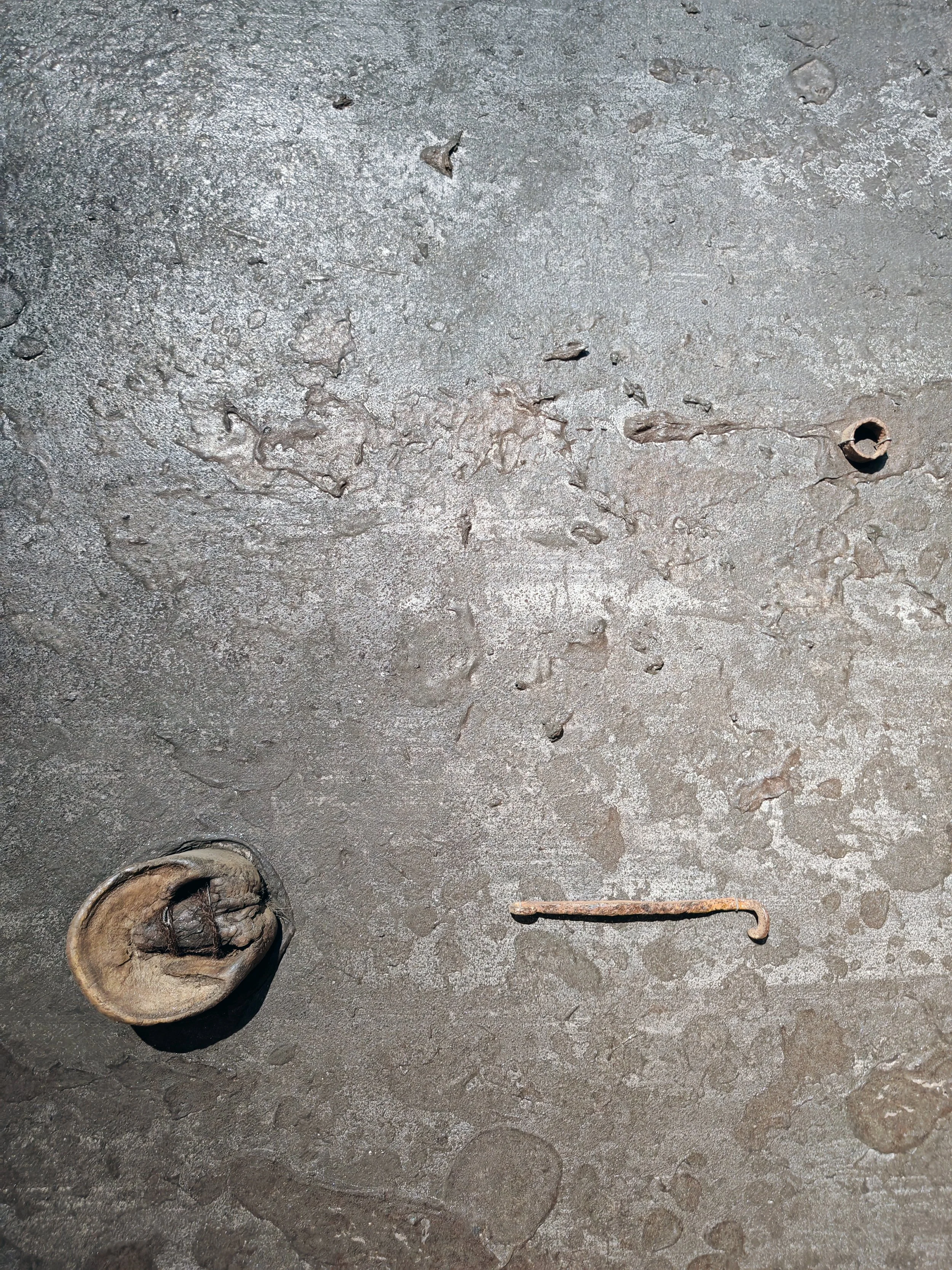 A weathered, rusty metal surface with various old, corroded tools and objects including a circular object, a hook, a screw, and other small metal parts scattered across the surface.