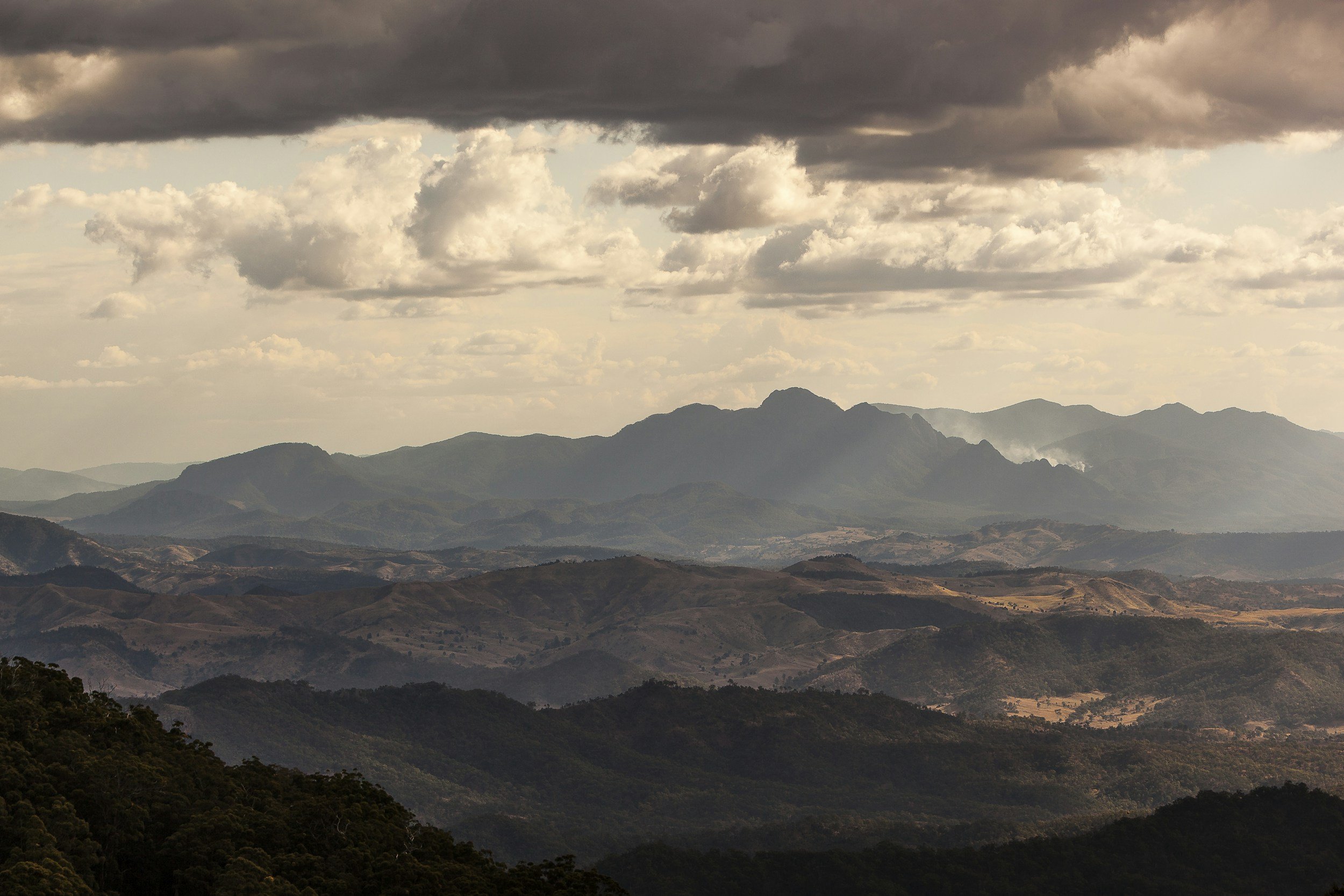 Landscape of rolling hills and mountains with a cloudy sky overhead.