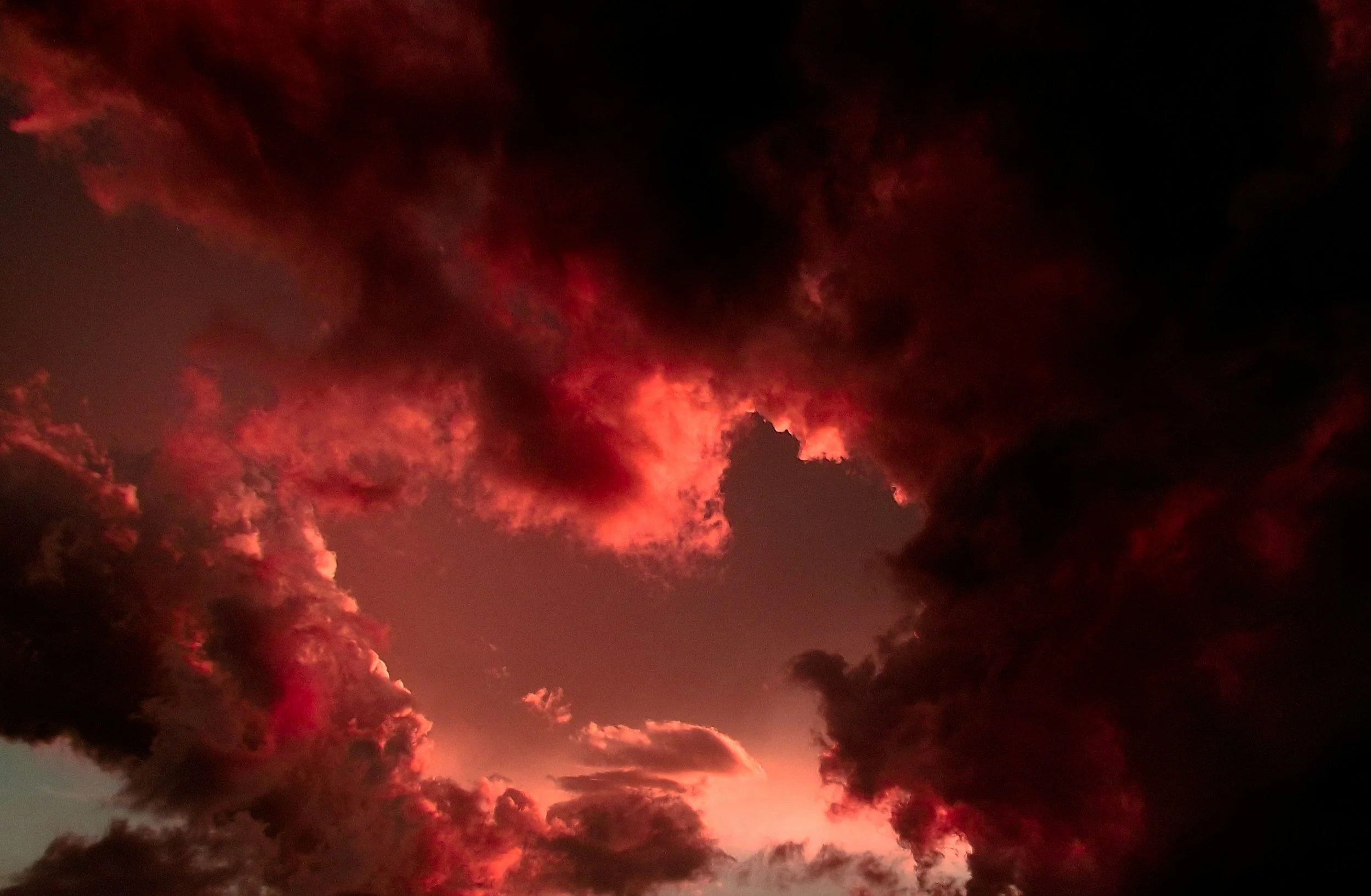 Dark clouds illuminated with fiery red and orange hues in the sky during sunset or sunrise.