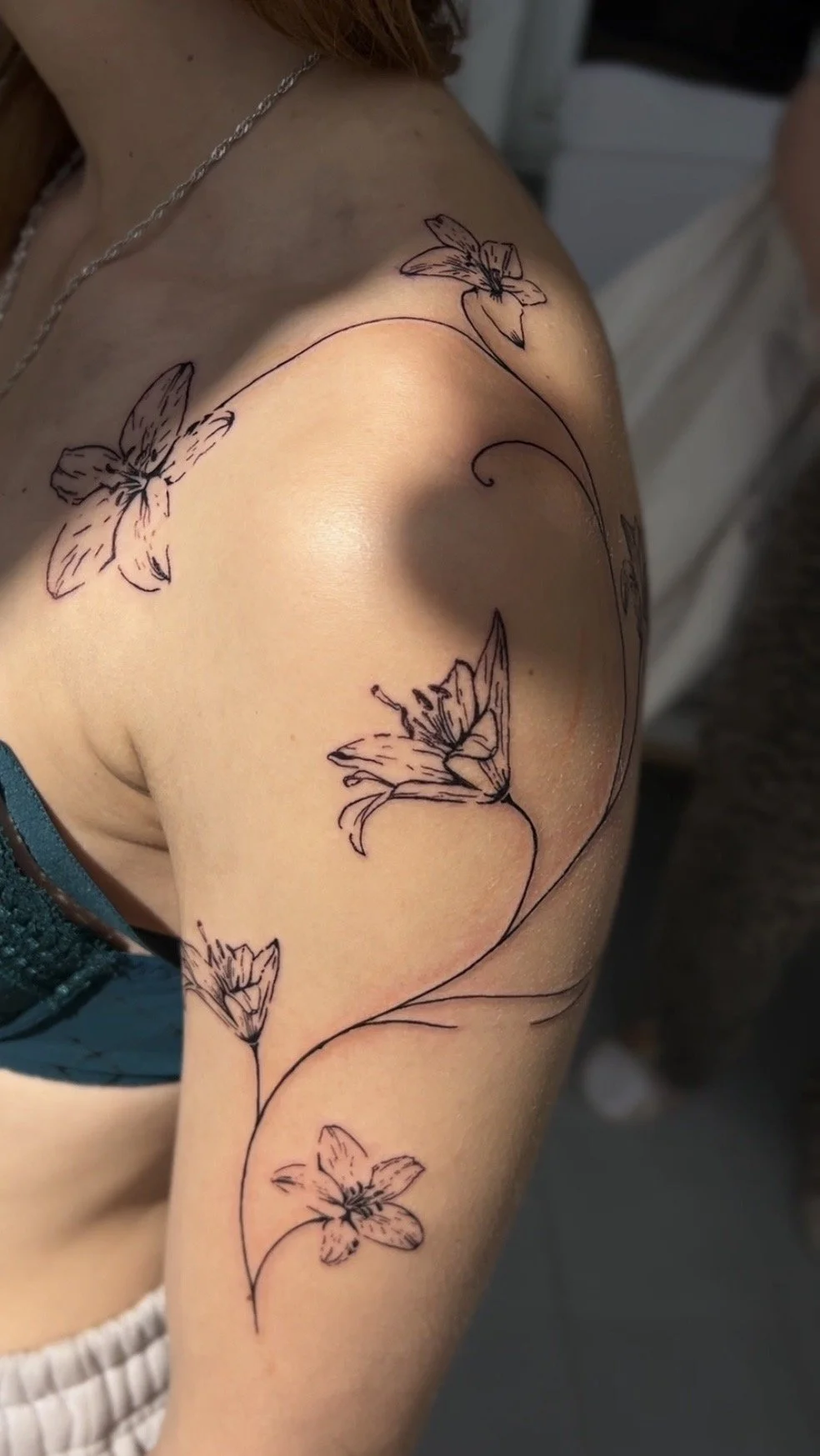 Schwarze Brusttattoo mit Blüten- und Schmetterlingsdesign auf der Schulter und Oberarm.