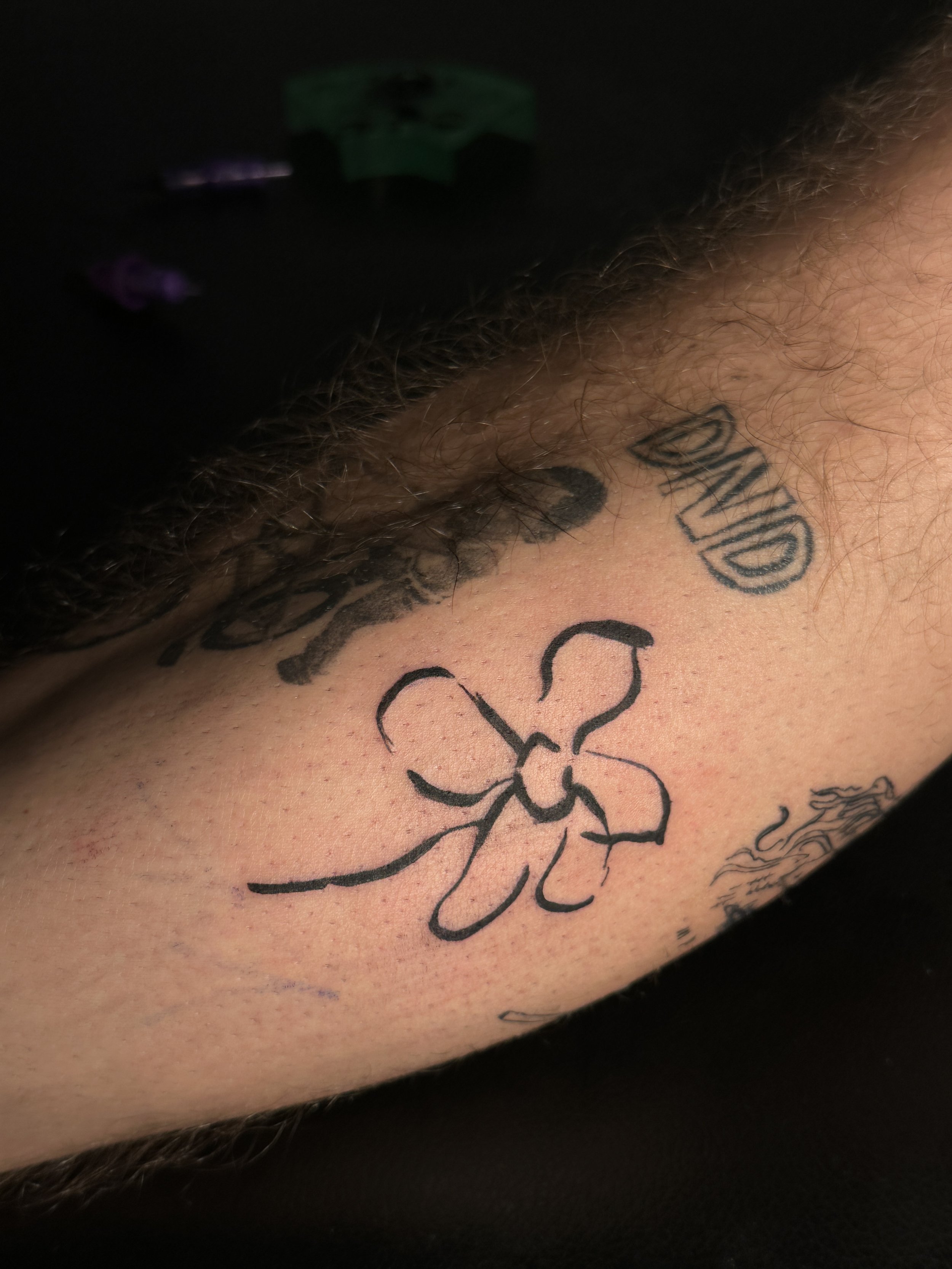 Nahaufnahme eines Tattoos auf der Haut, das eine stilisierte Blume und den Text 'LOVE' zeigt.