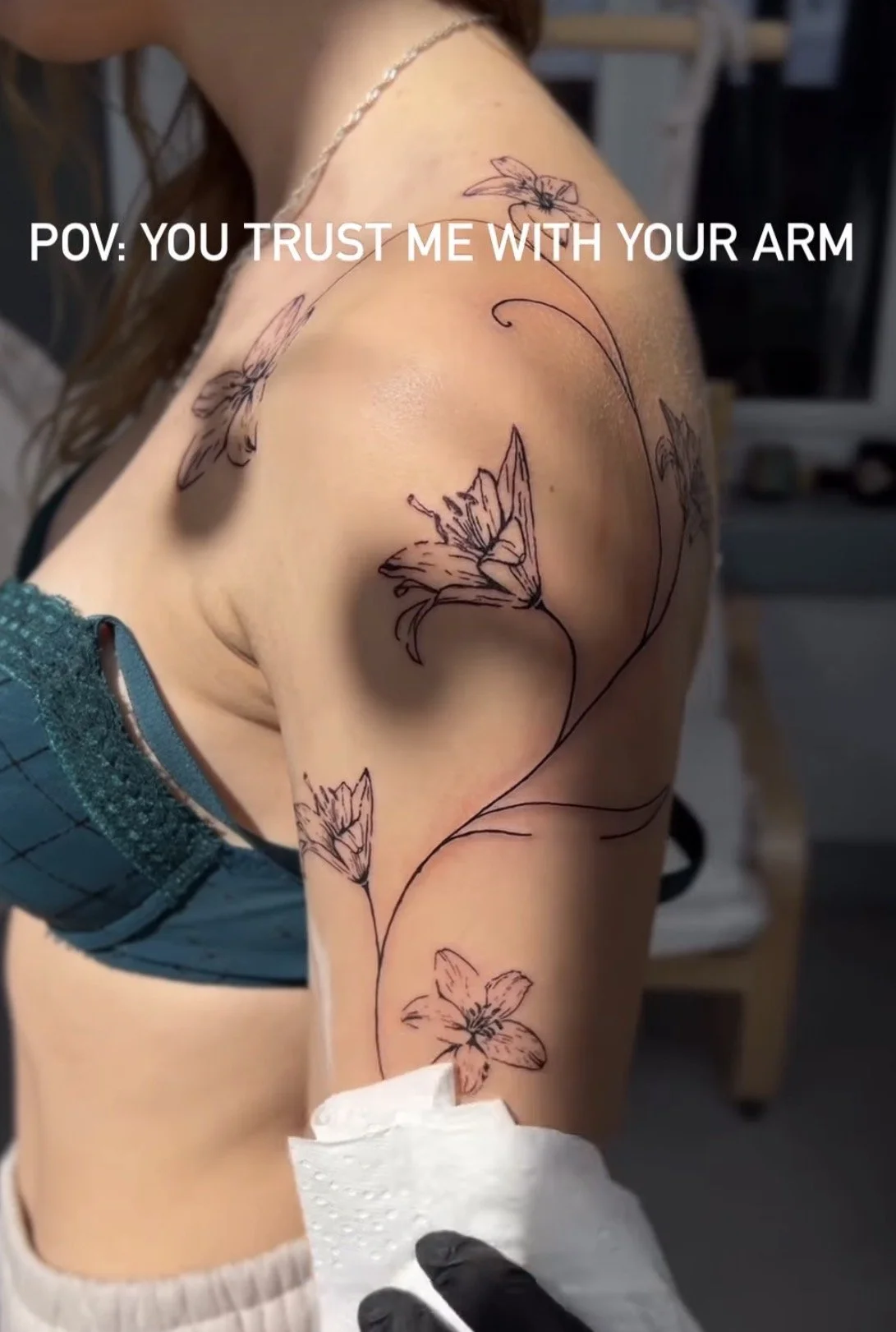 Tattoo mit Blumen auf dem Schulterbereich einer Person, die in einem Steharbeitsplatz eine Tätowierung bekommt.