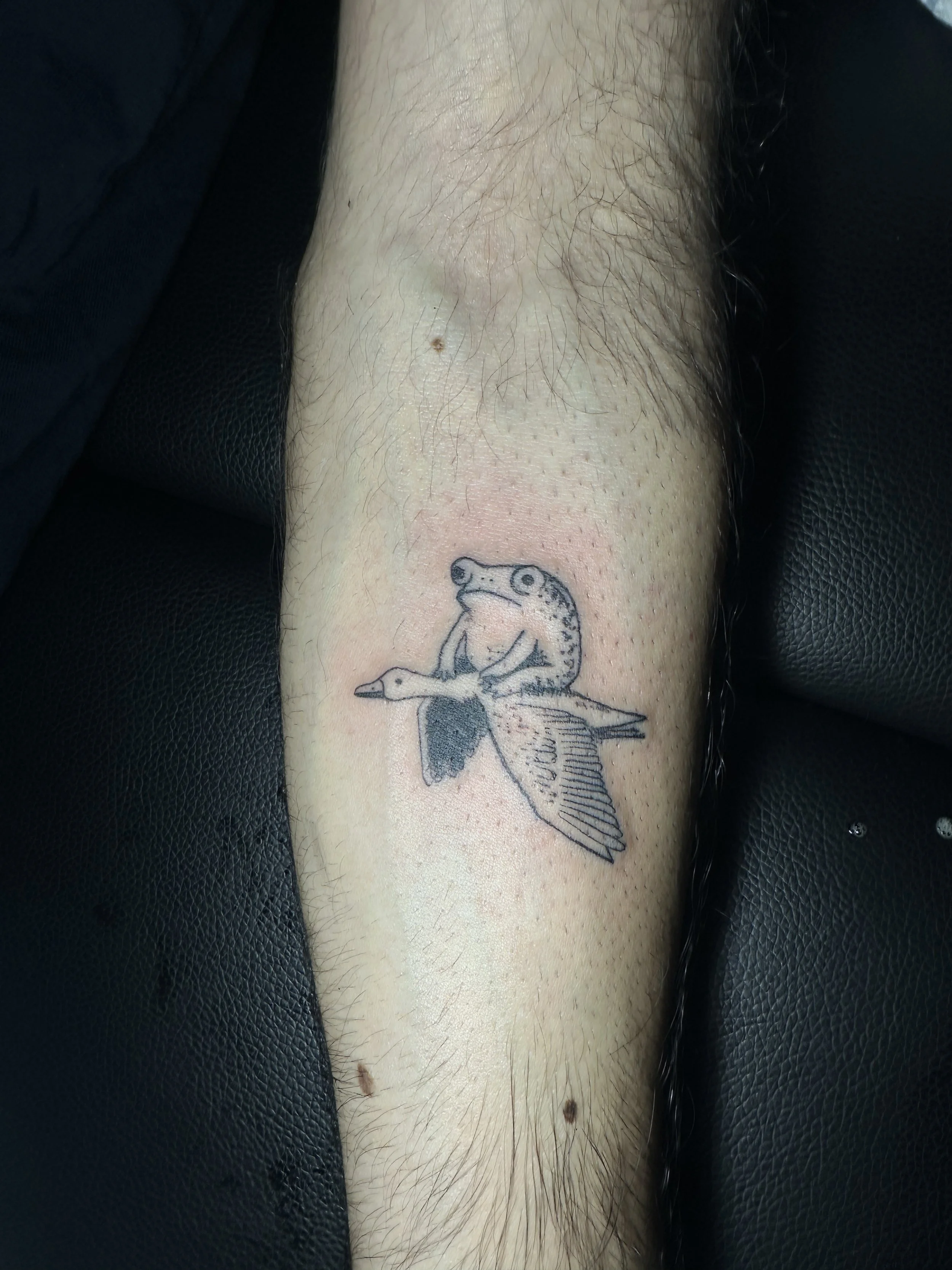 Nahaufnahme eines Beins mit einer Tattoo eines Frosches, der auf einem Vogel sitzt.