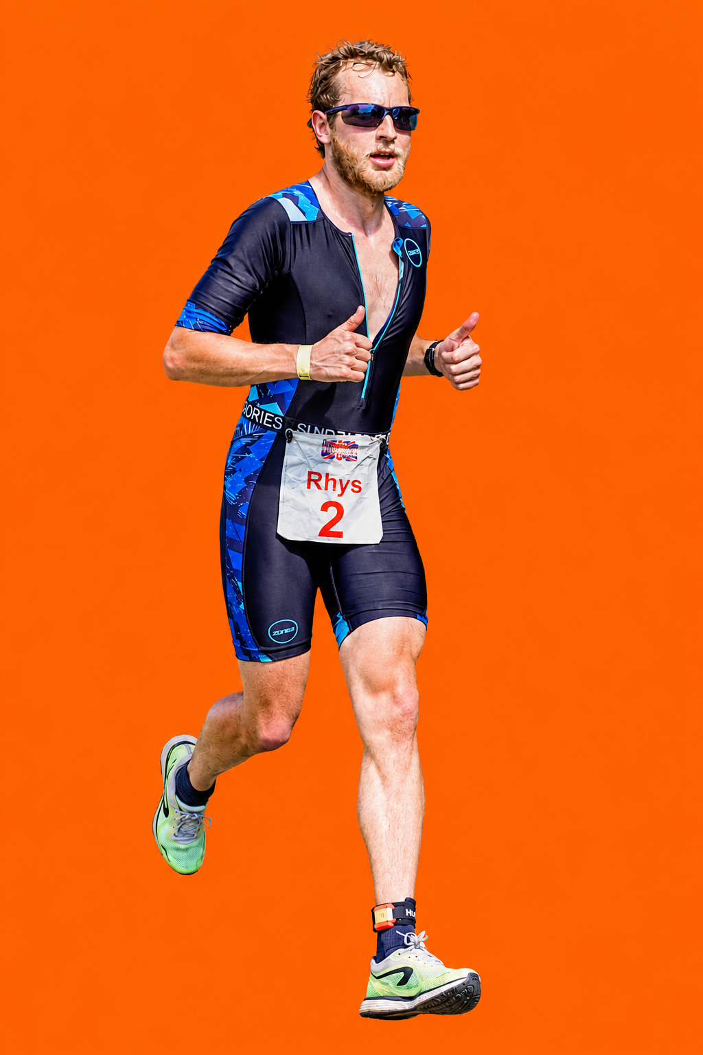 A male runner with a beard, sunglasses, and wearing a blue and black athletic suit with a race number 'Rhys 2', running on a bright red background with text about Rhys Williamson's second place finish.