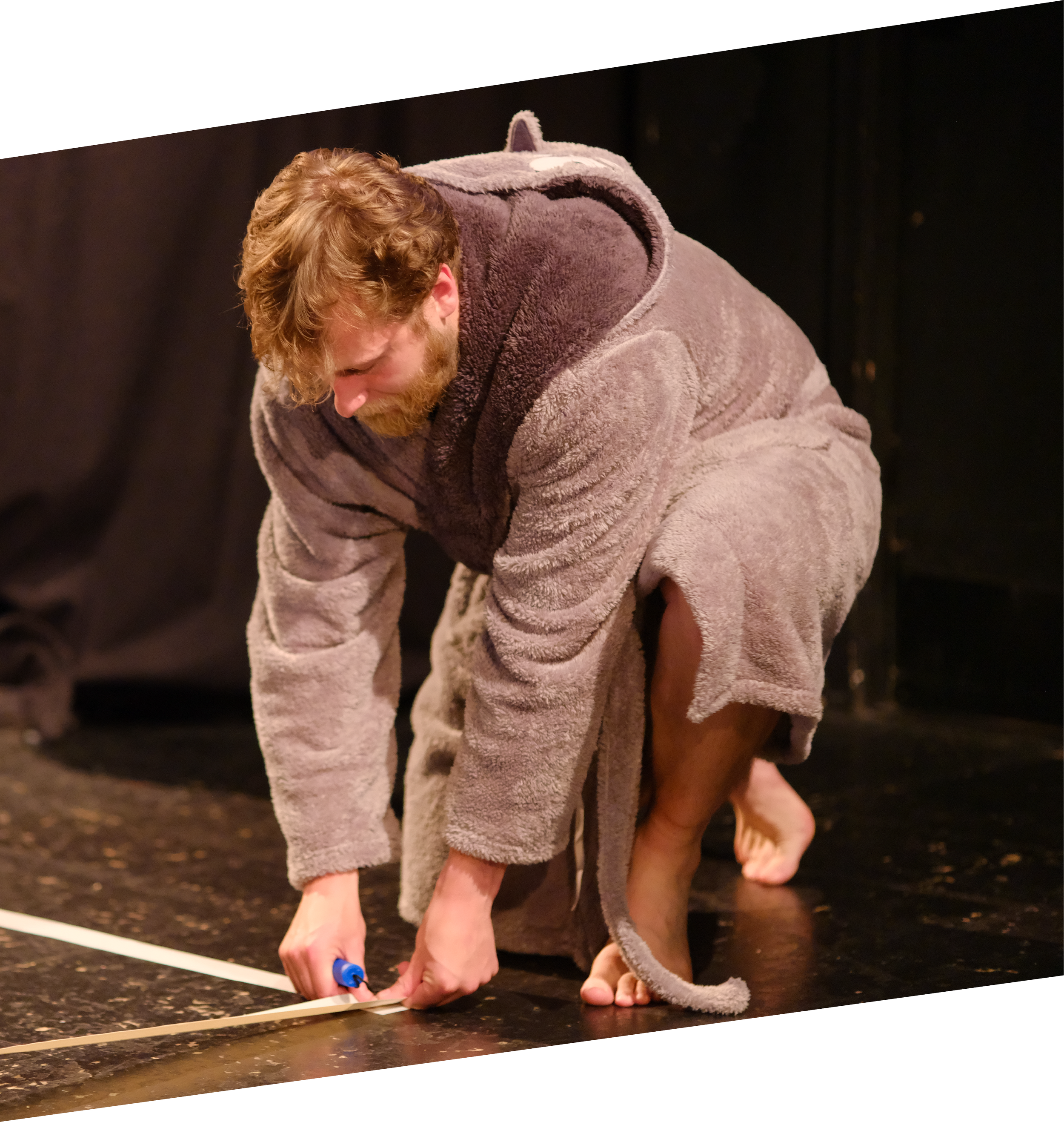 Person in a gray hoodie and shorts kneeling on a track, measuring or marking the ground with a marker, at night.