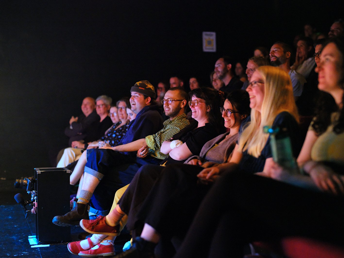Audience sitting in theater, smiling and laughing during a performance.
