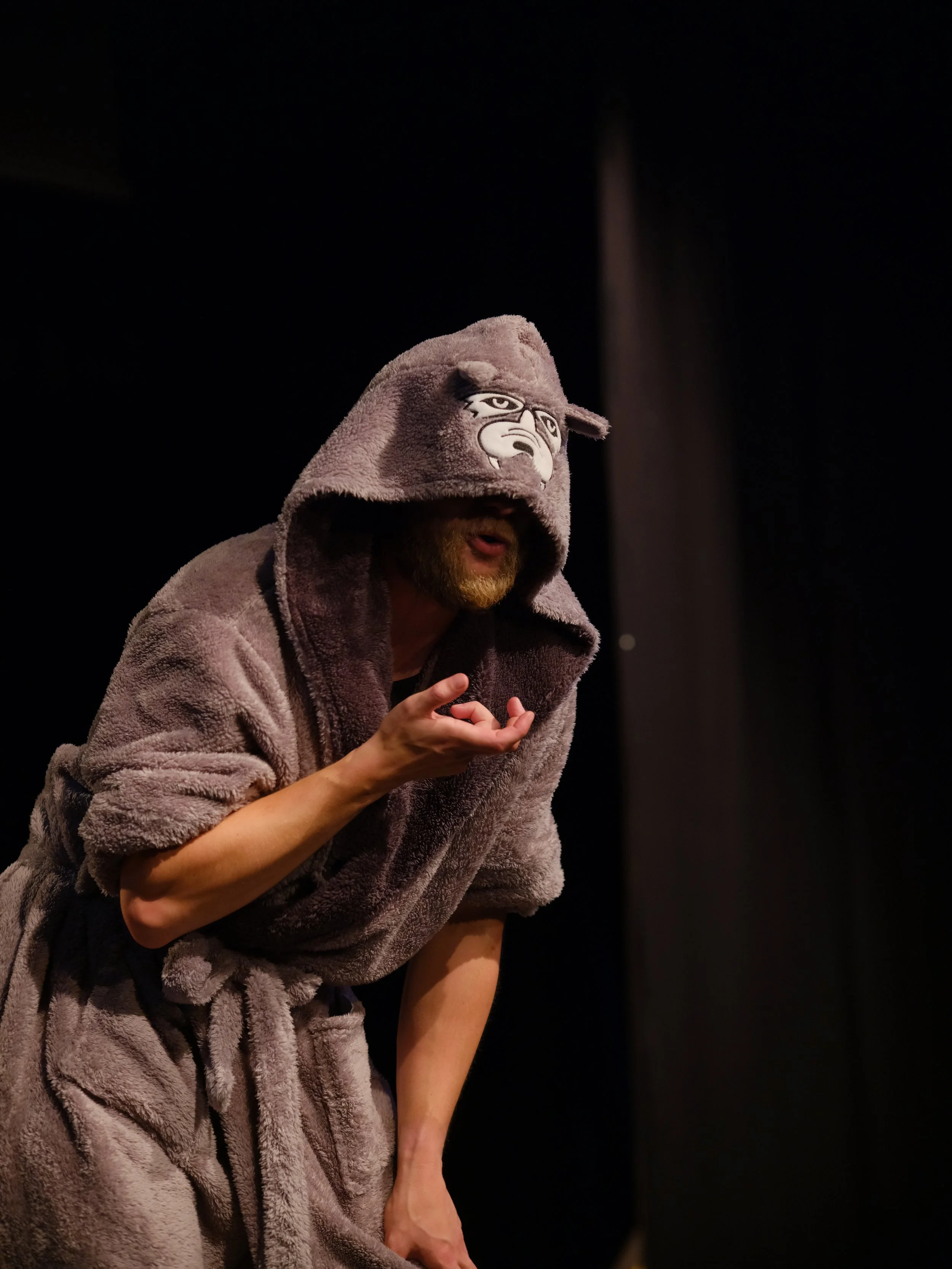 Person wearing a grey hoodie with a cartoon face, leaning forward with hand near face, against a dark background.