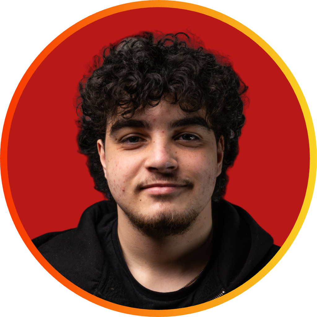 Young man with curly dark hair and light facial hair, wearing a black hoodie, against a red background.
