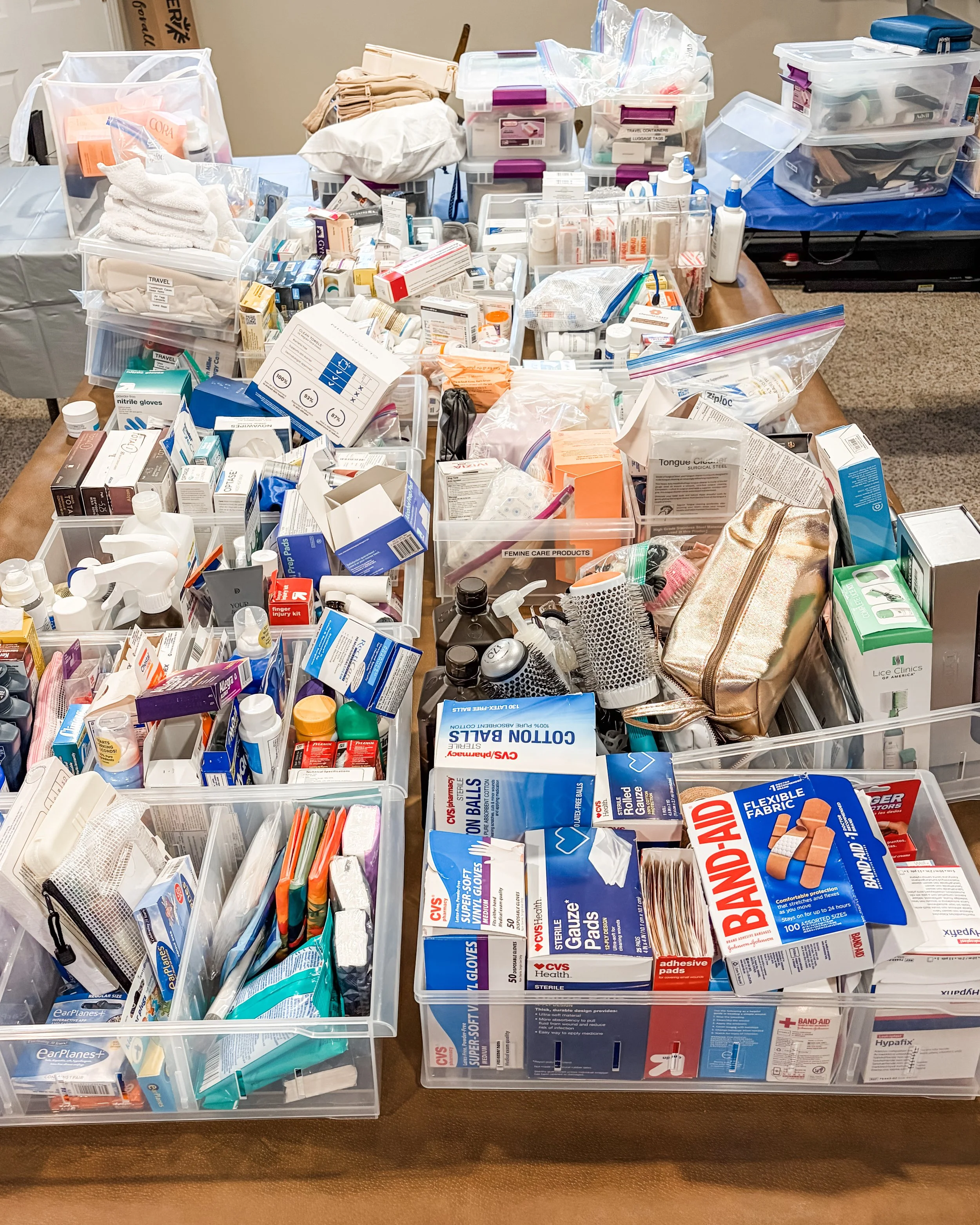 A table filled with medical supplies and organization containers, including bandages, gauze, gloves, topical creams, medicine boxes, and toiletry items, all neatly arranged in plastic bins and bags.