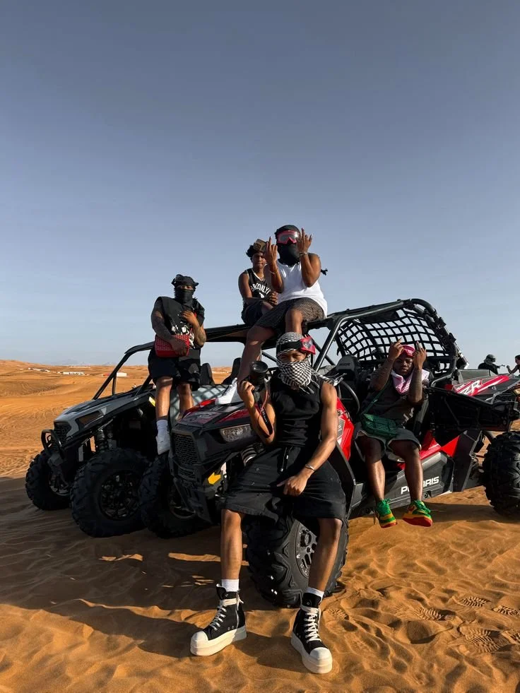 Group of five people wearing protective gear and masks posing on and around an off-road vehicle in a desert.